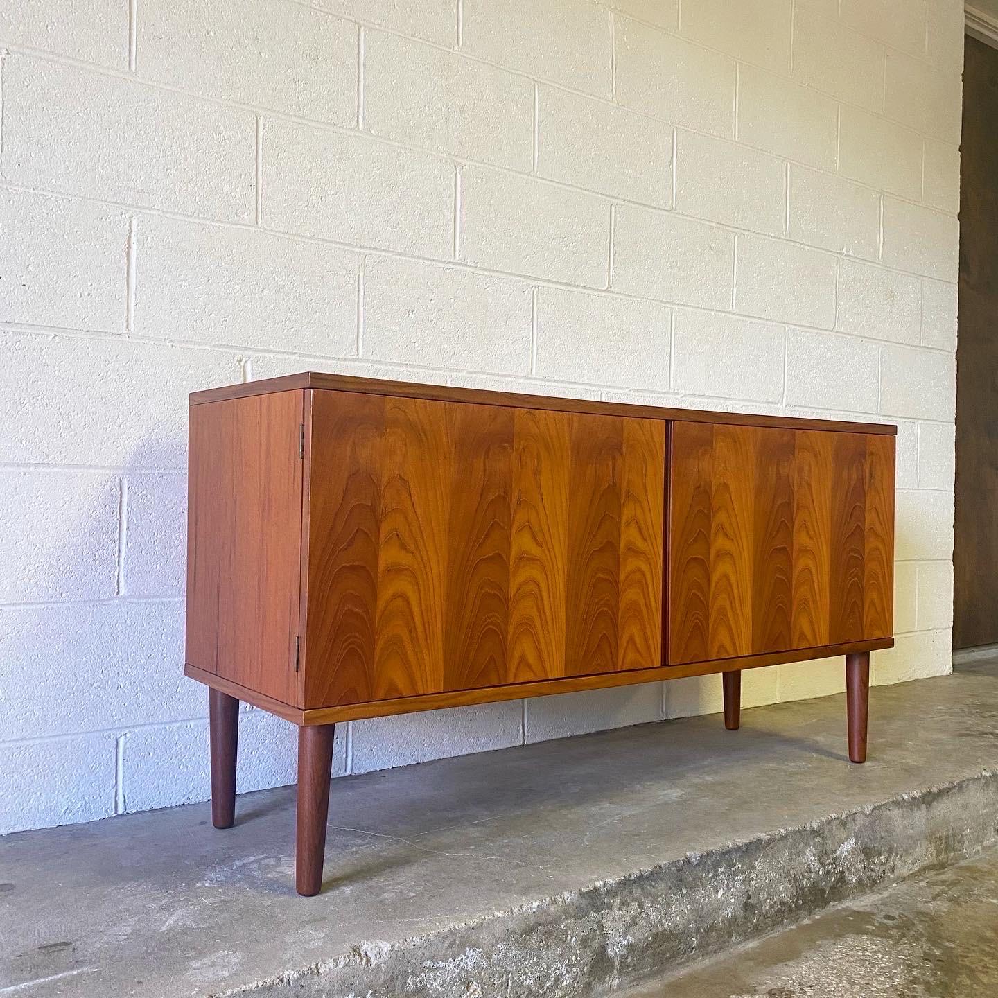 This is a great teak sideboard, buffet or credenza designed by Hans Olsen, made in Denmark ca. 1960’s. This beautifully crafted piece displays opposing teak veneers and brass fittings. Doors swing open to reveal adjustable shelving. Perfect for an