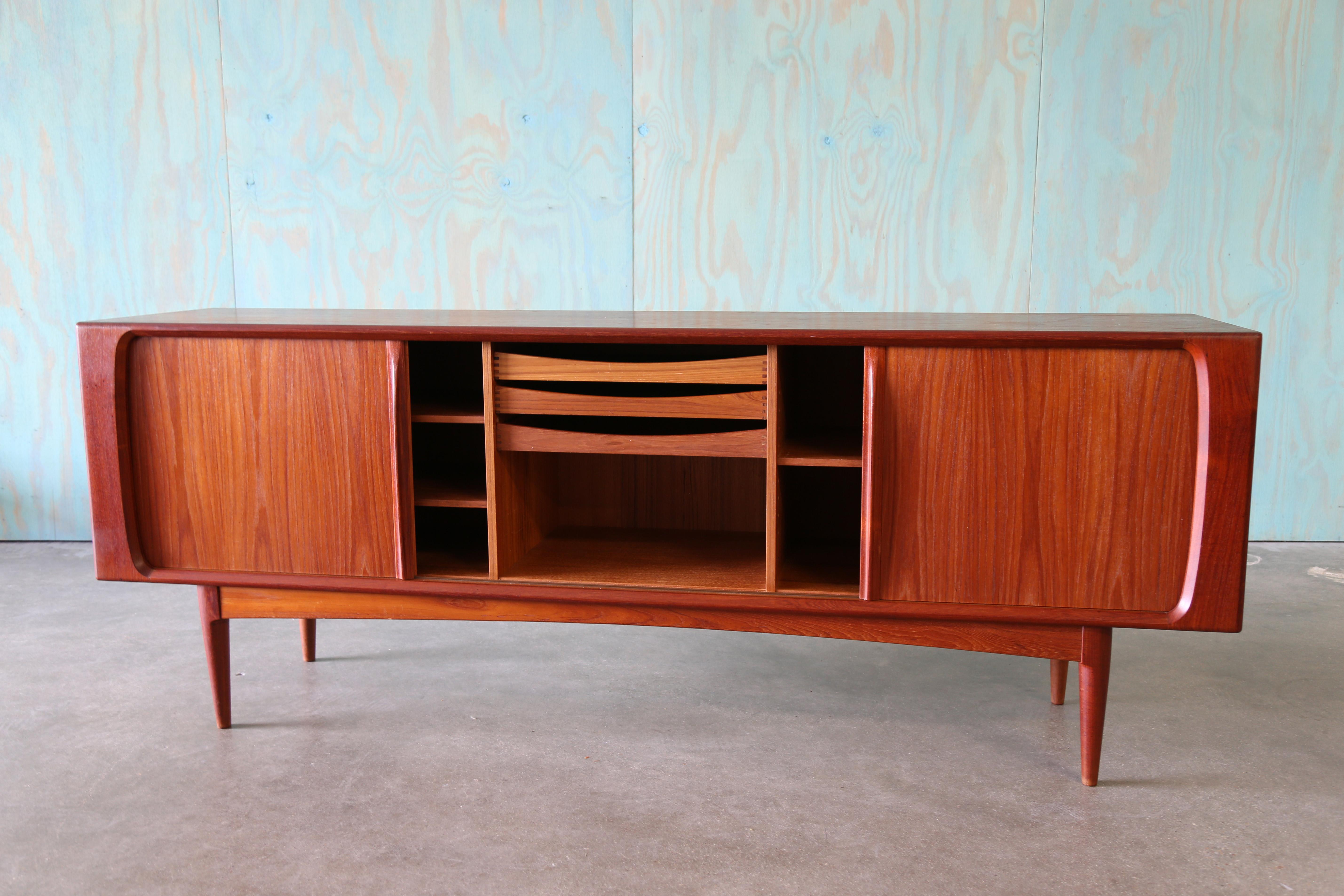 Un aparador moderno danés de teca diseñado por los famosos ebanistas Bernhard Pedersen & Son e importado de Dinamarca.  El aparador tiene puertas de persiana que se deslizan fácilmente para mostrar cajones extraíbles y estanterías abiertas