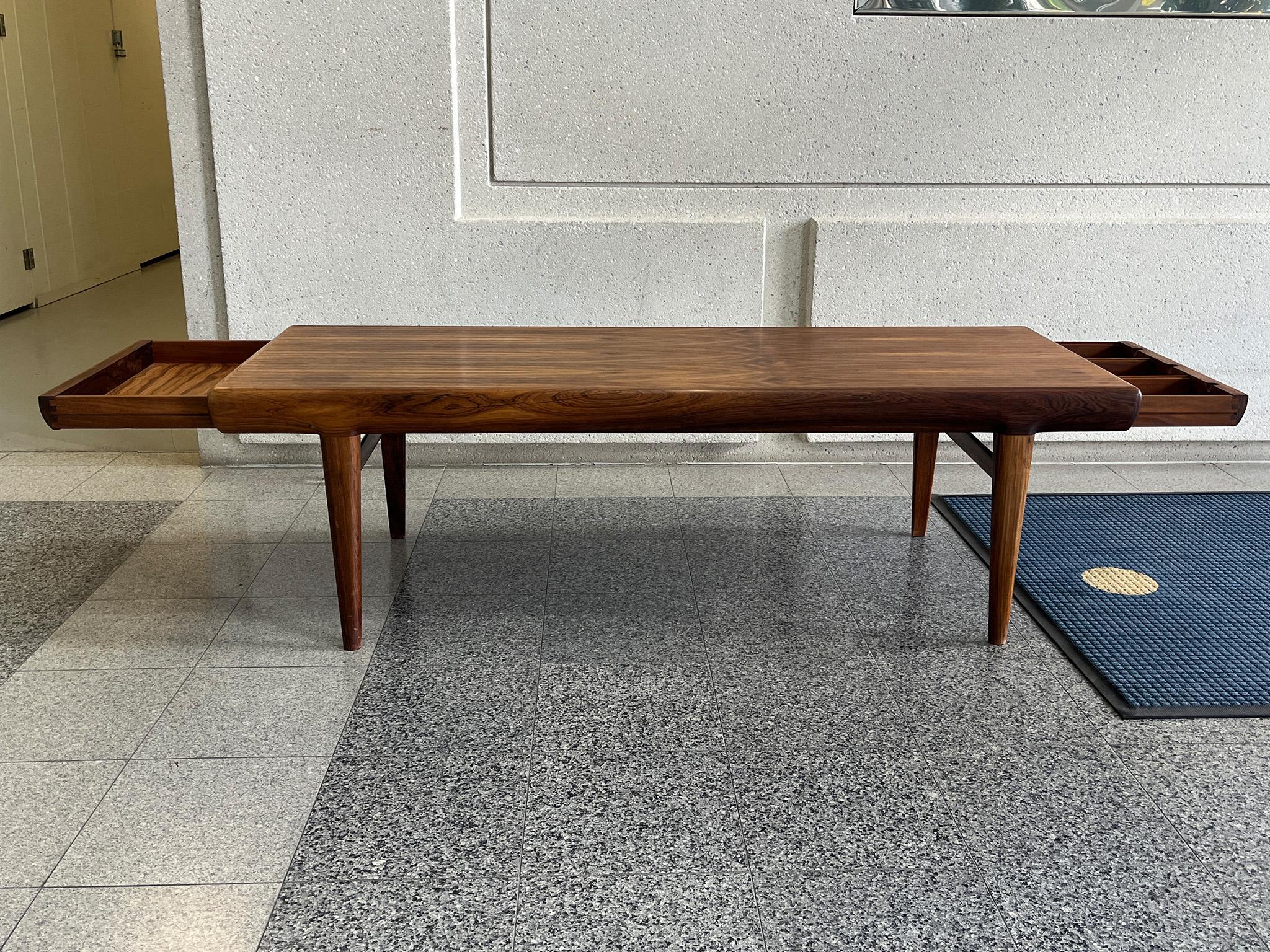 Stylish 1960s Danish Modern Coffee Table by important furniture designer Johannes Andersen for CFC Silkeborg. The table was crafted with gorgeous bookmatched Rosewood veneers, and is characterized by its tapered legs, two functional drawers, and