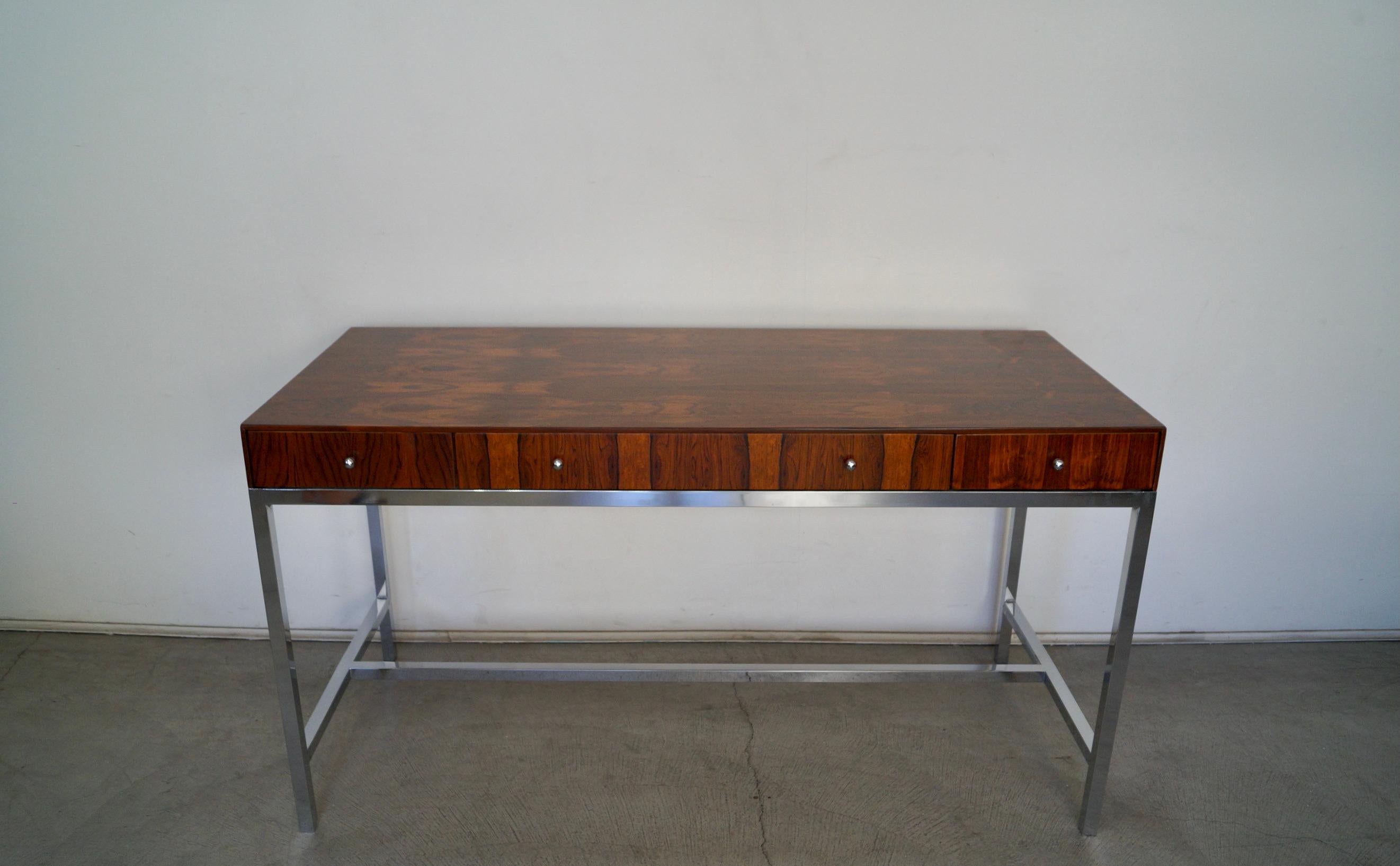 Vintage 1960's Mid-century Modern rosewood desk for sale. It has been professionally refinished, and looks stunning. The chrome base has been polished and is also in excellent top shape. It has a clean design with three drawers and chrome knobs.