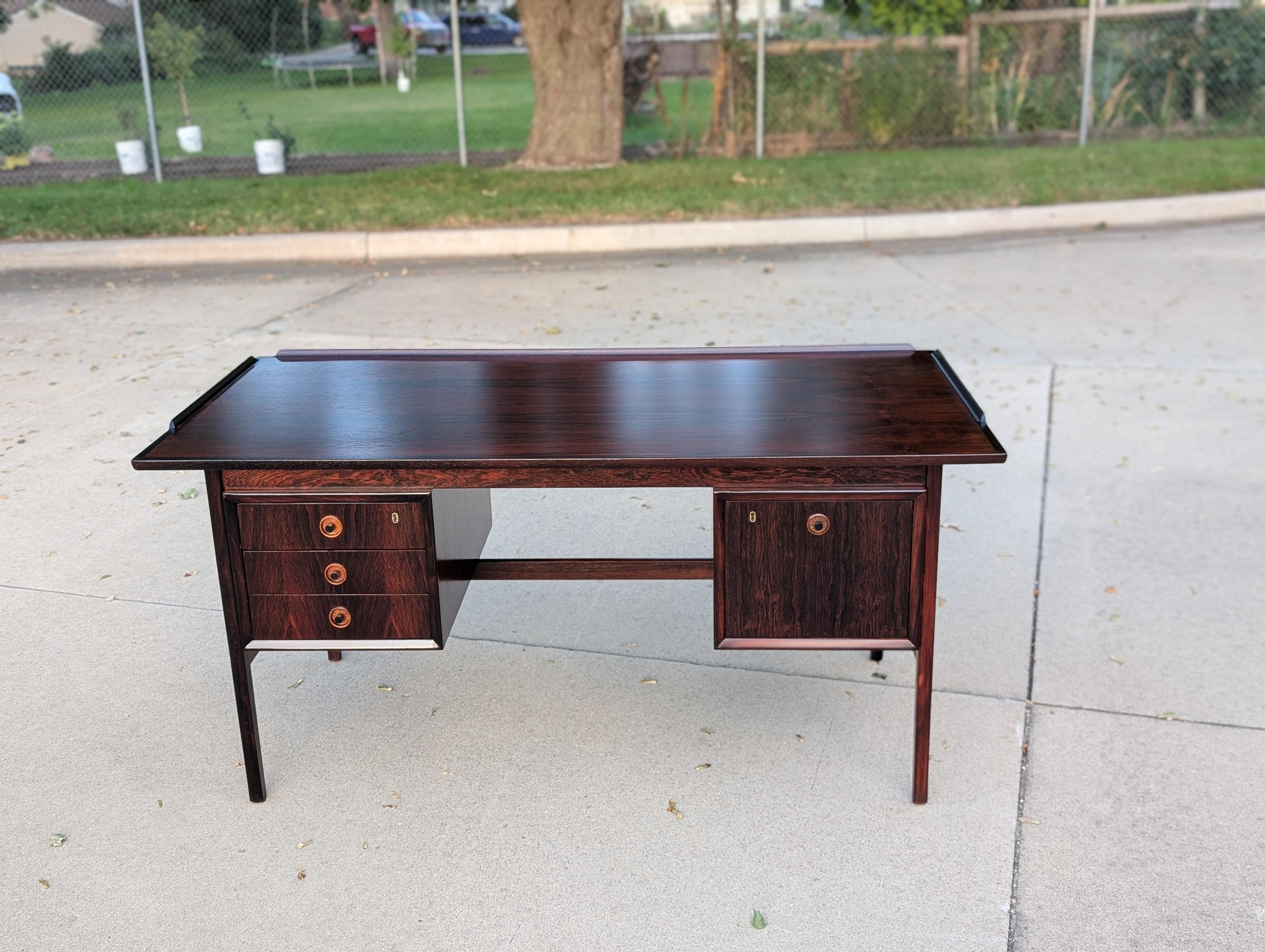 1960s Danish modern desk in rosewood.

Exceptional rosewood color and grain throughout.

Clean mahogany dovetail drawers with small solid tapered wood pulls. Three drawers on left, one large file drawer on right.

Working locks and key. Brass lock