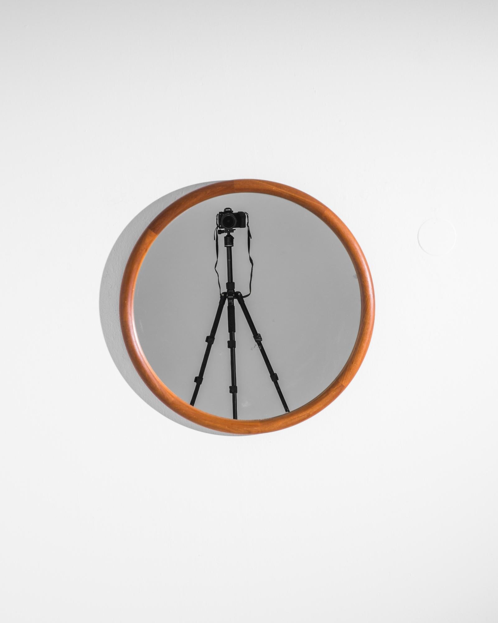 This stylish Mid-Century Modern mirror made in Denmark circa 1960 flaunts immaculate circularity, the teak frame merging into glass like a lunar eclipse. Exuding the charm of Nordic simplicity, this vintage mirror easily adapts to contemporary