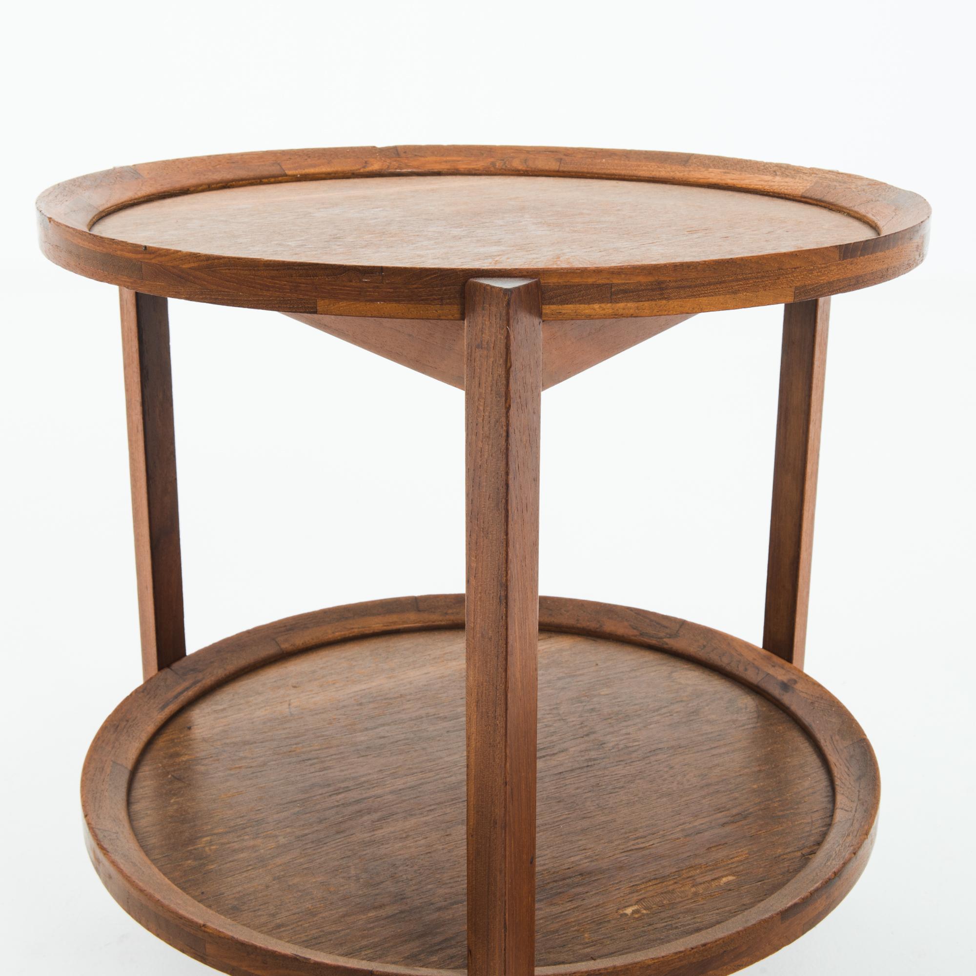 This wooden bar cart was made in Denmark, circa 1960. It features an elegant construction of geometric forms, reflecting the clean lines of Danish Modern design. The two circular tiers are accompanied by an oblique raised edge, and three triangular