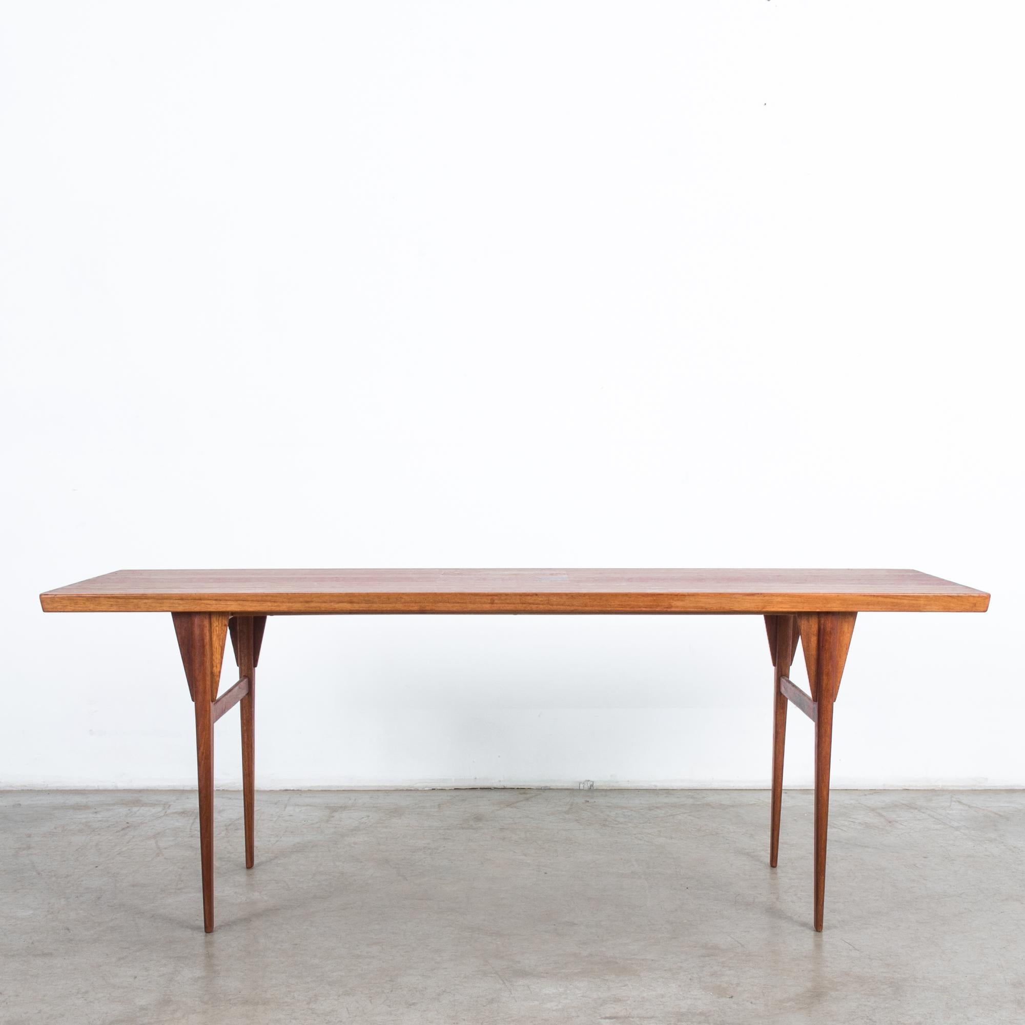 This wooden coffee table was made with a warm tone in Denmark, circa 1960. The rectangular tabletop features a beautiful bookmatched wood grain pattern, resonant mirrored teak. Tapered legs with triangular brackets and side stretchers support this