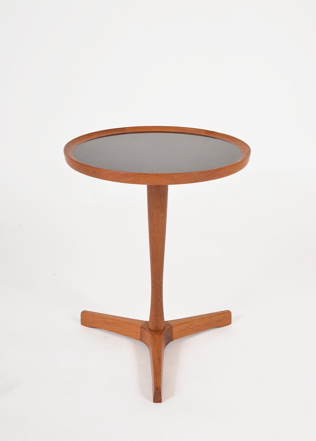 This perfectly proportioned Danish tripod base side table was designed by Hans C. Andersen for Artex. This is a lovely example of Danish Modern design. Its shaft and base are of solid teak, and the tabletop is inlaid with black mica laminate. The