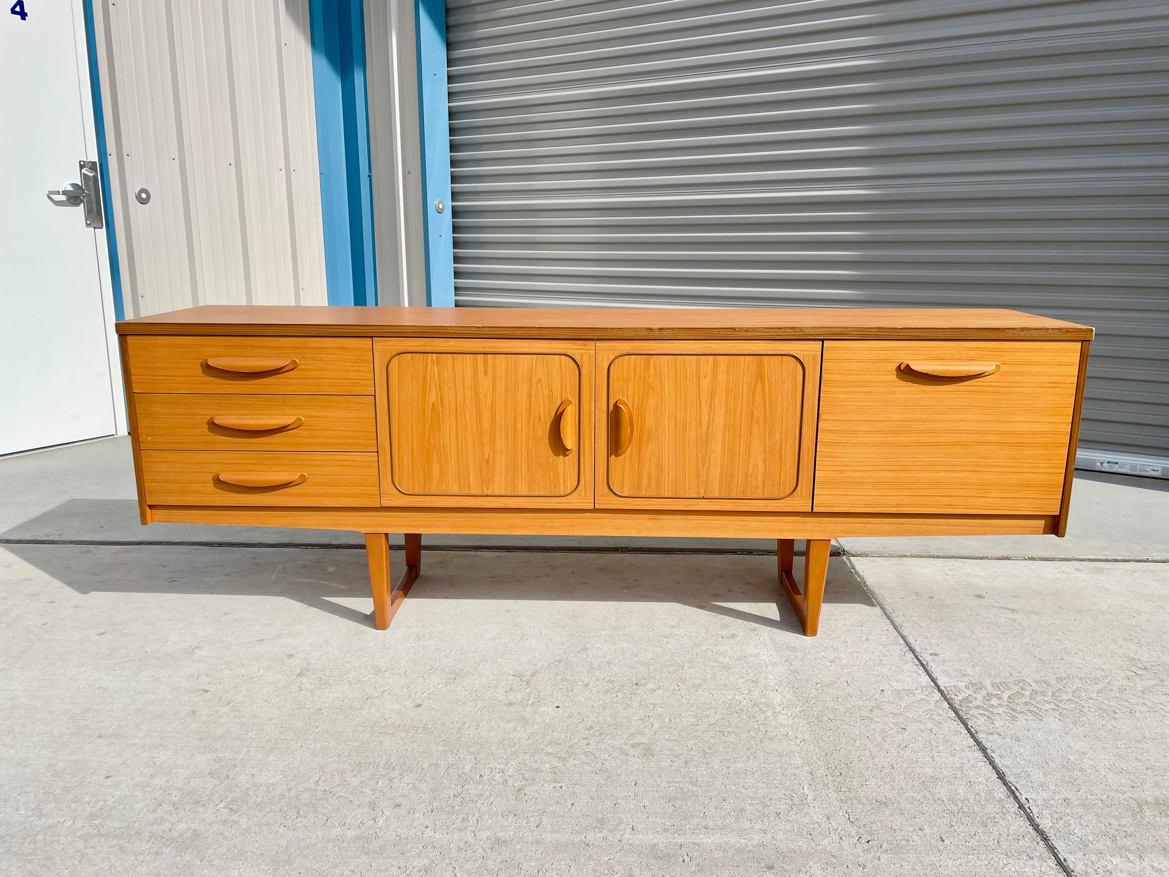 This fantastic danish modern teak credenza was designed and manufactured by Drylund in Denmark circa 1960s. This danish modern credenza features three pull-out drawers and a center two-door cabinet with lovely sculpted handles giving it an extra