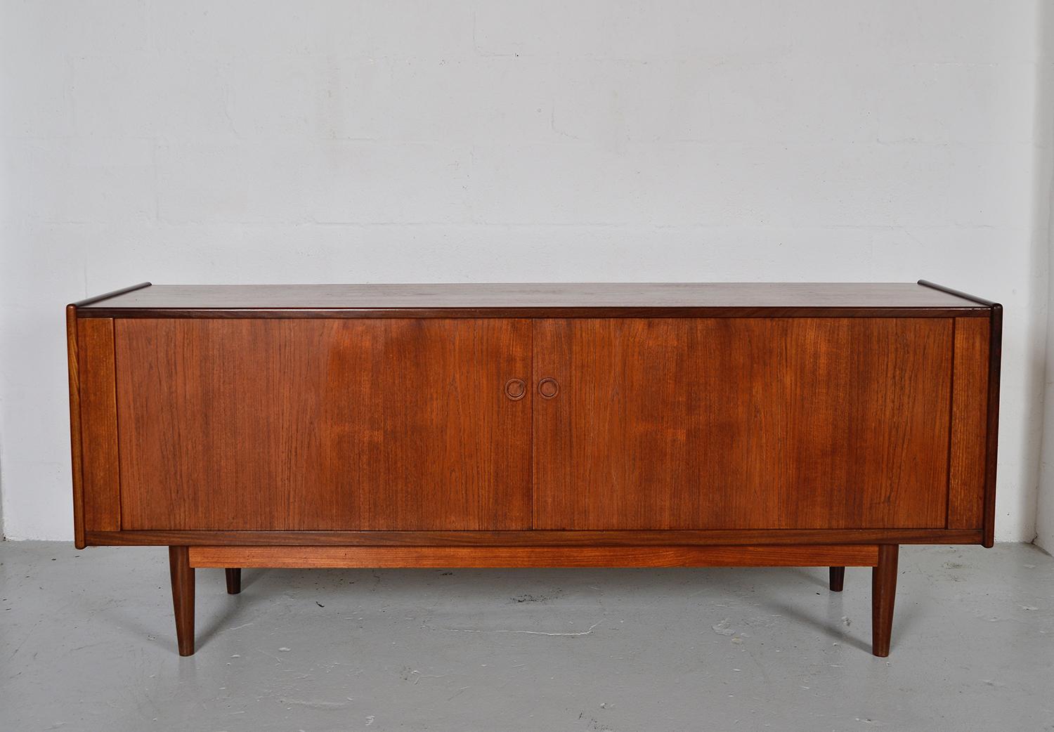 Early 1960s Danish modern teak sideboard with unusual full width sliding tambour doors, which consist of precise machined teak slats set on a thick oil cloth that slide along tracks, and disappear into the unit itself. This is a very nicely made
