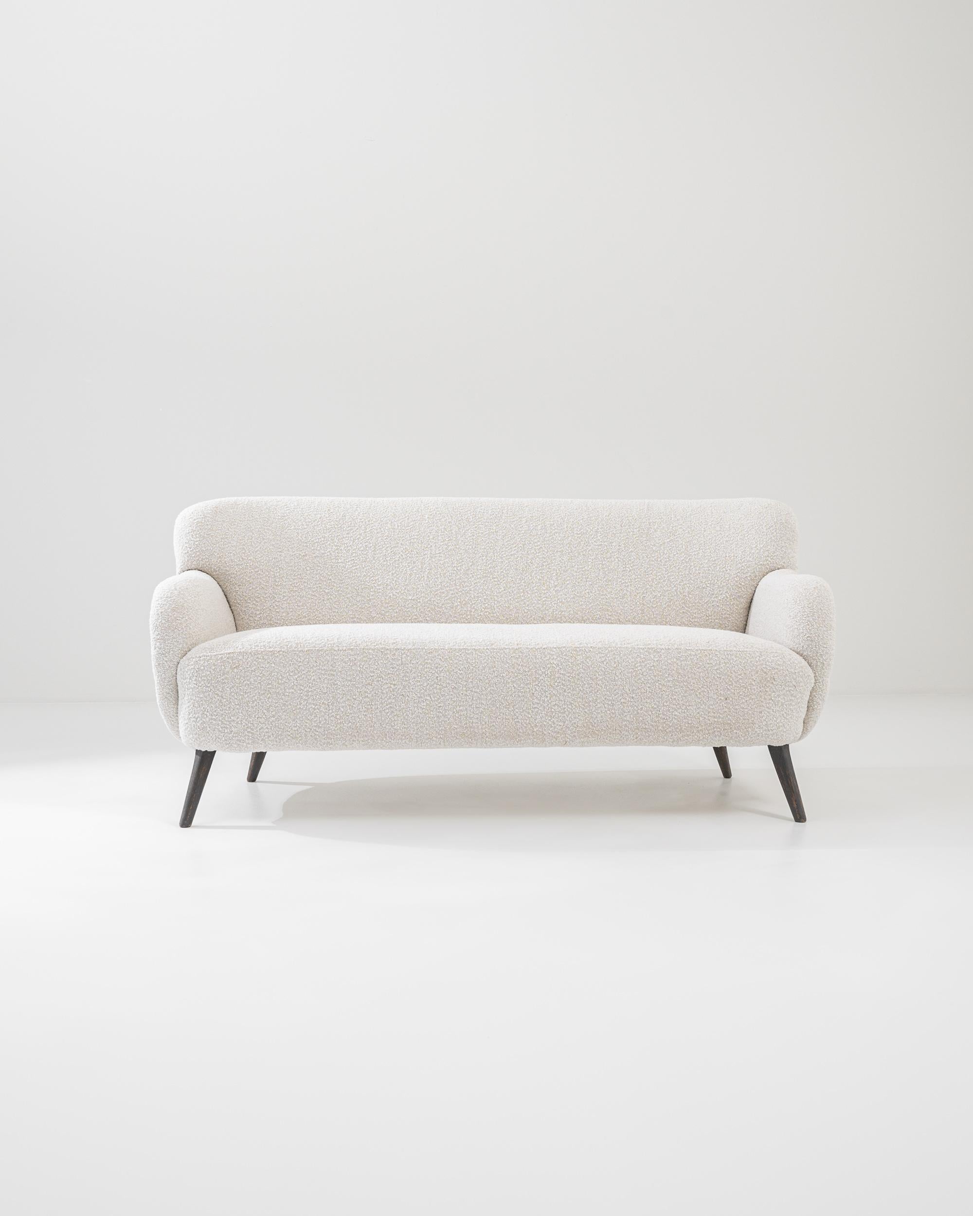 Effortlessly simple, this 1960s sofa embodies the homey elegance of Danish Modern furniture. The curves of the cushioned seat, backrest and armrests have a cloud-like softness, accentuated by the textural white boucle of the upholstery. Tapered