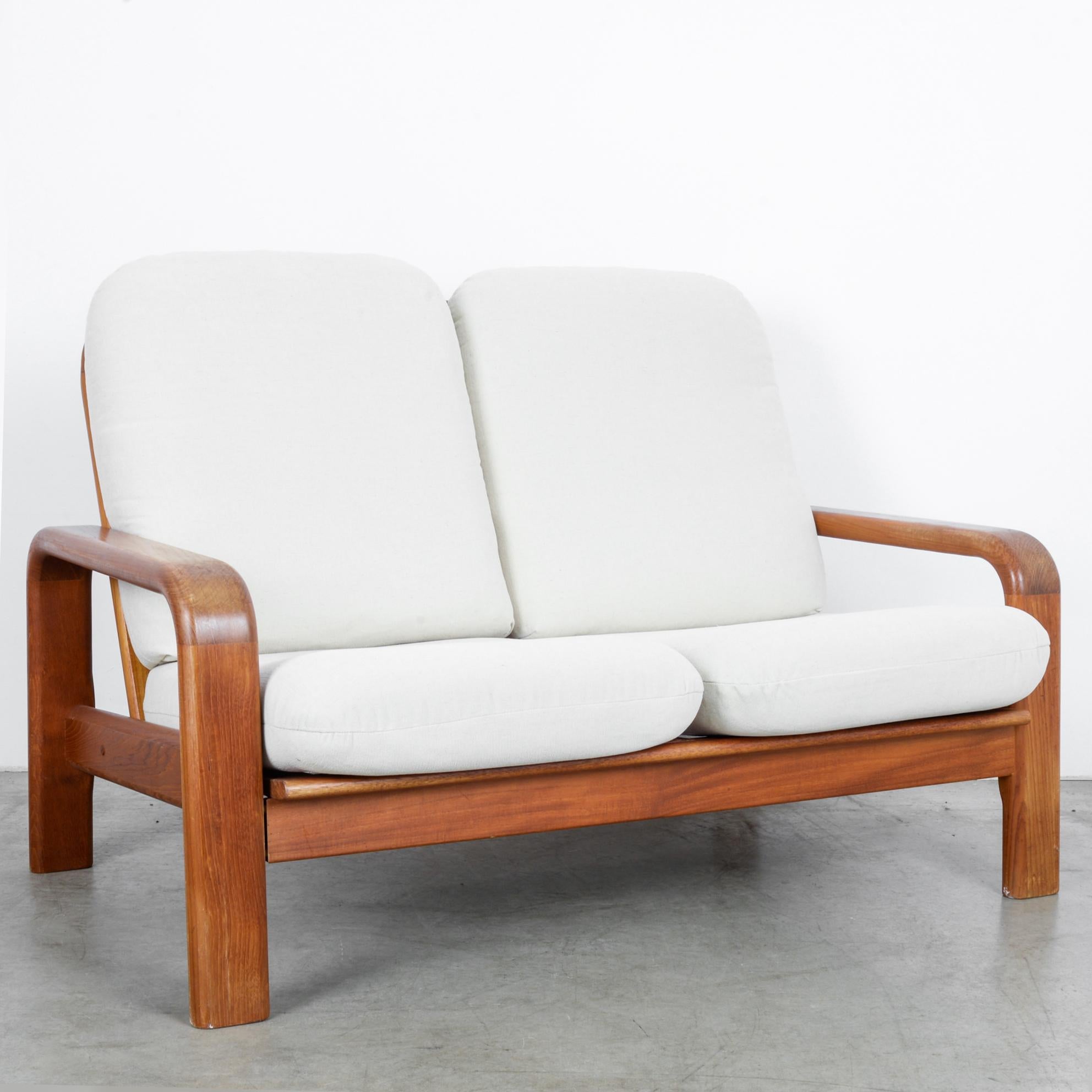 This two-seat sofa was made in Denmark, circa 1960. The ivory white upholstered seats and backrests provide comfort and enhance the warm tones of the polished wood. The armrests and backrests feature rounded edges, which form a pleasing contrast