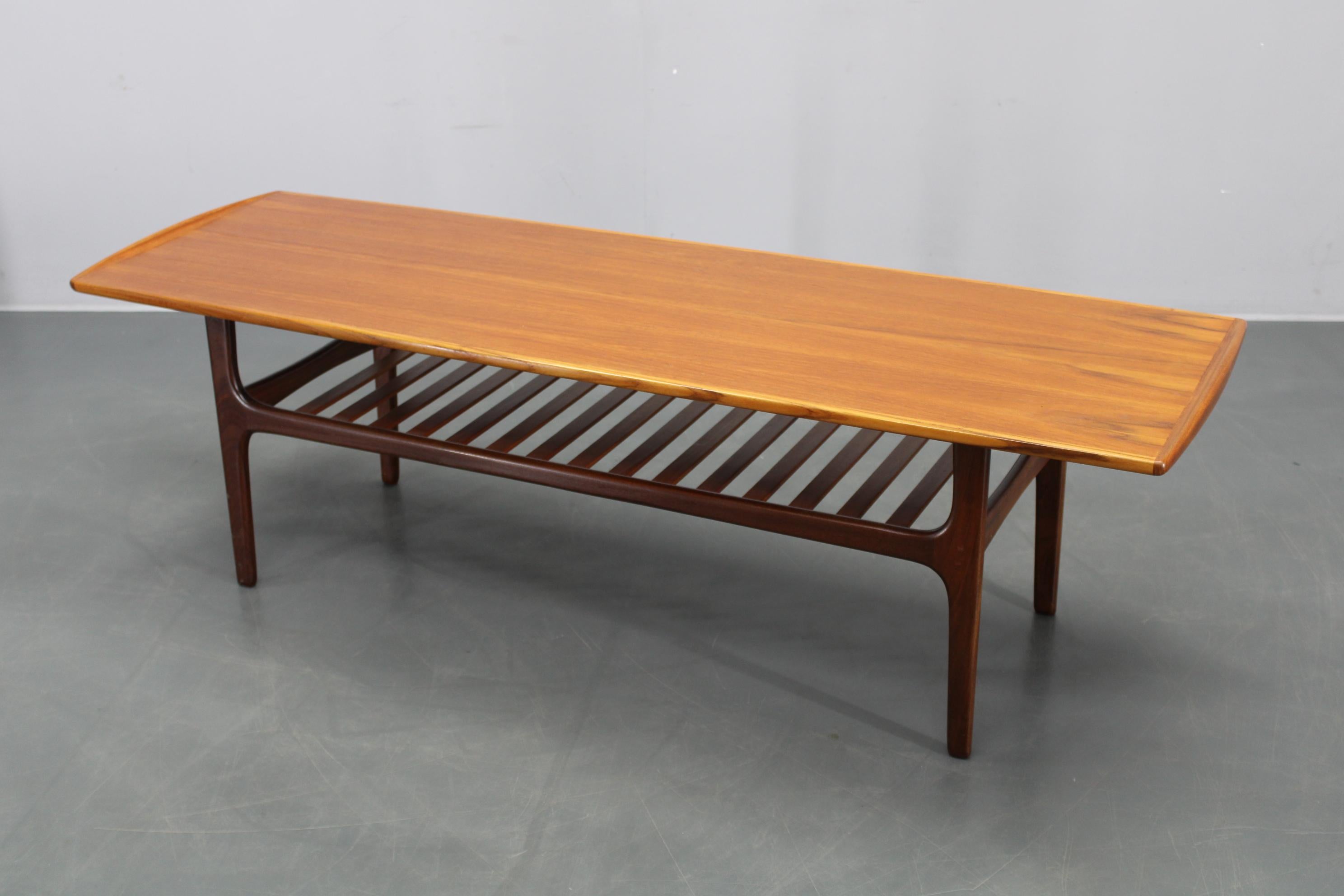 Beautifully restored Danish coffee table from the 1960s, featuring a solid teak base and a teak veneered top, with elegantly sculpted edges and a slatted magazine shelf below. 
  This piece combines iconic Scandinavian design and craftsmanship,