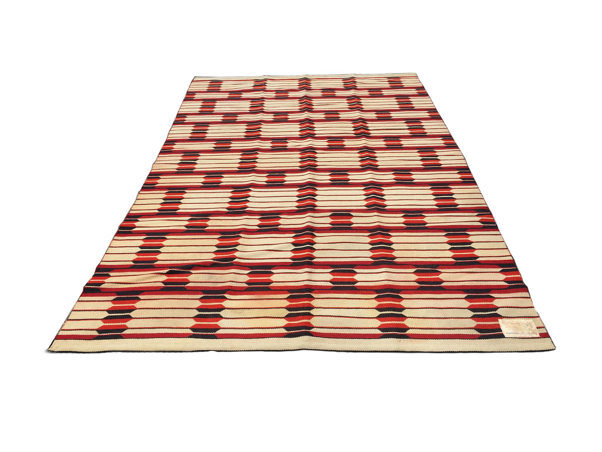 A Danish modern flat-weave rug designed and made exclusively for Bloomingdale's, 1960s. It is remarkable for its dynamic patterns of interlocking geometric shapes in a rich palette of red, black, and beige white. The rug is reversible which