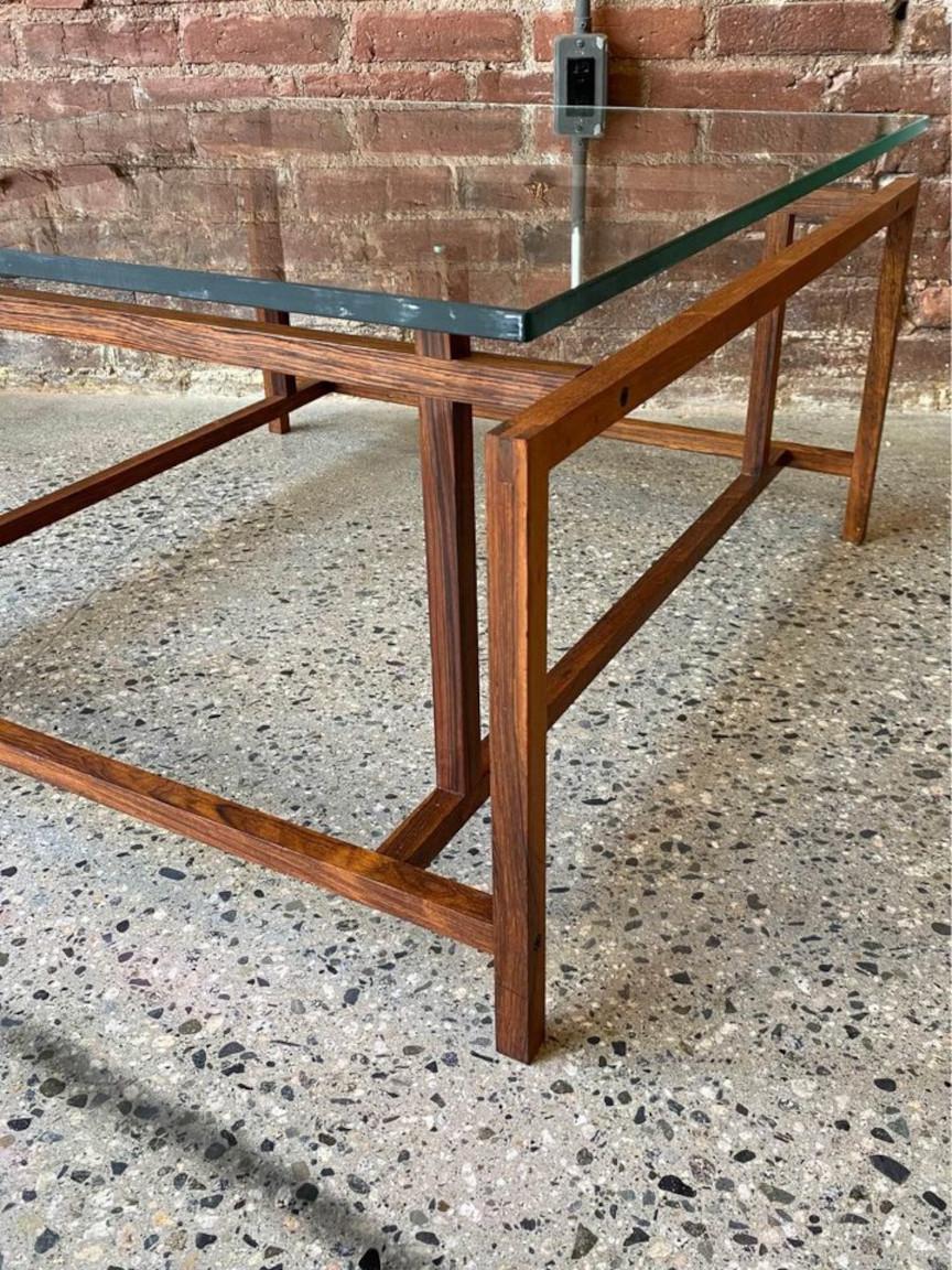 Exquisite 1960s Danish coffee table designed by Henning Norgaard for Komfort. This masterpiece showcases a captivating geometric construction, a robust Brazilian rosewood frame, precise finger-jointed craftsmanship, and a substantial glass tabletop.