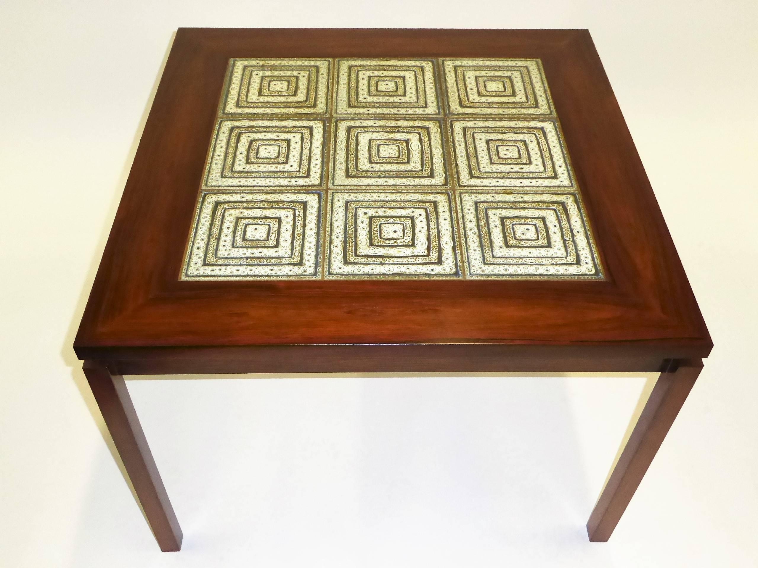 Beautifully figured Rosewood highlights this table as well as the centered Nils Thorsson tiles, probably Royal Copenhagen. Cantilevered positioned legs add to its charm, extending out from the apron frieze, the top overhanging like an eave. Restored