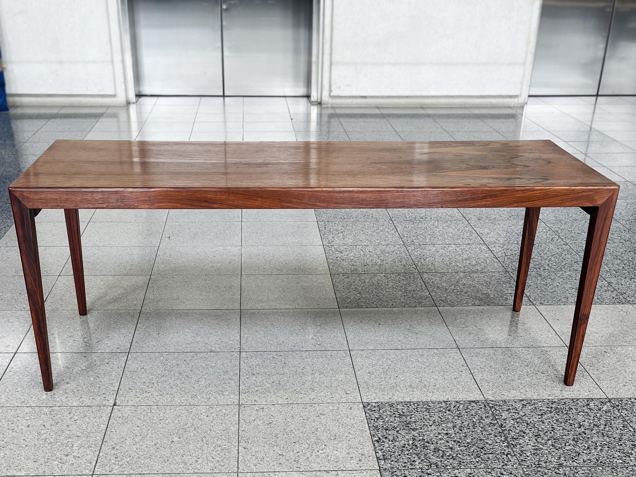 Une élégante table basse moderne danoise en bois de rose. Le design se caractérise par des lignes épurées et des bords arrondis. Un plateau étroit et des pieds hauts qui s'affinent vers le bas créent une impression de continuité et d'ouverture. Le