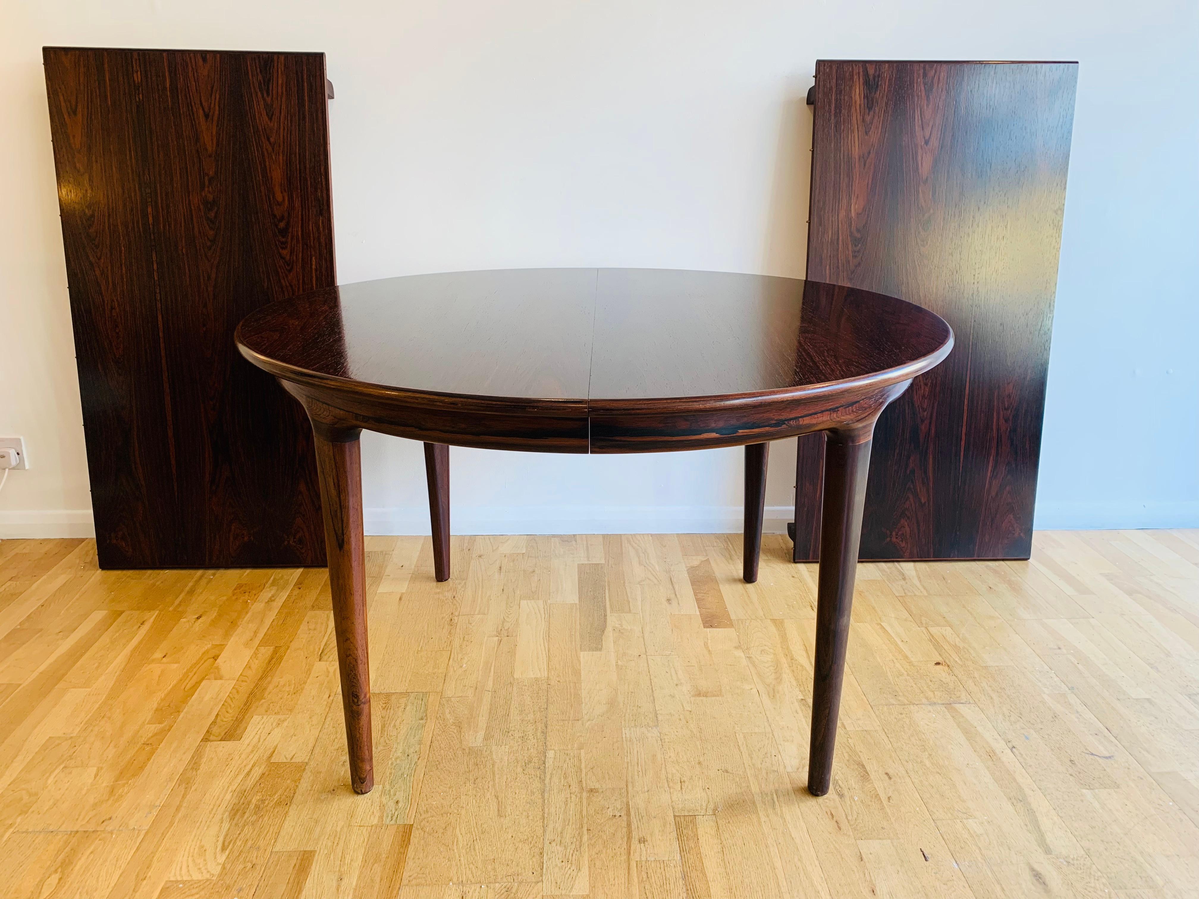 A stunning 1960s extendable rosewood dining table designed by Johannes Andersen for Uldum Møbelfabrik. The table features a veneered Rosewood top with solid tapered legs which slot into the underside of the table into the apron which seamlessly also