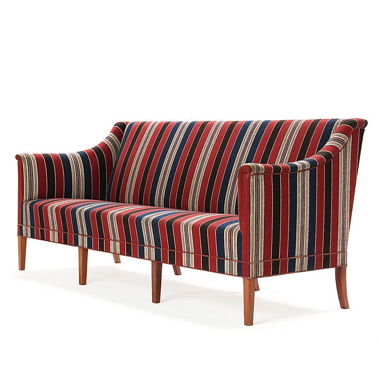 A majestic sofa having a sculptured body resting on eight (8) tapered mahogany legs, retaining the original red, navy and beige striped wool fabric. Designed in the 1940s and manufactured in the 1960s.