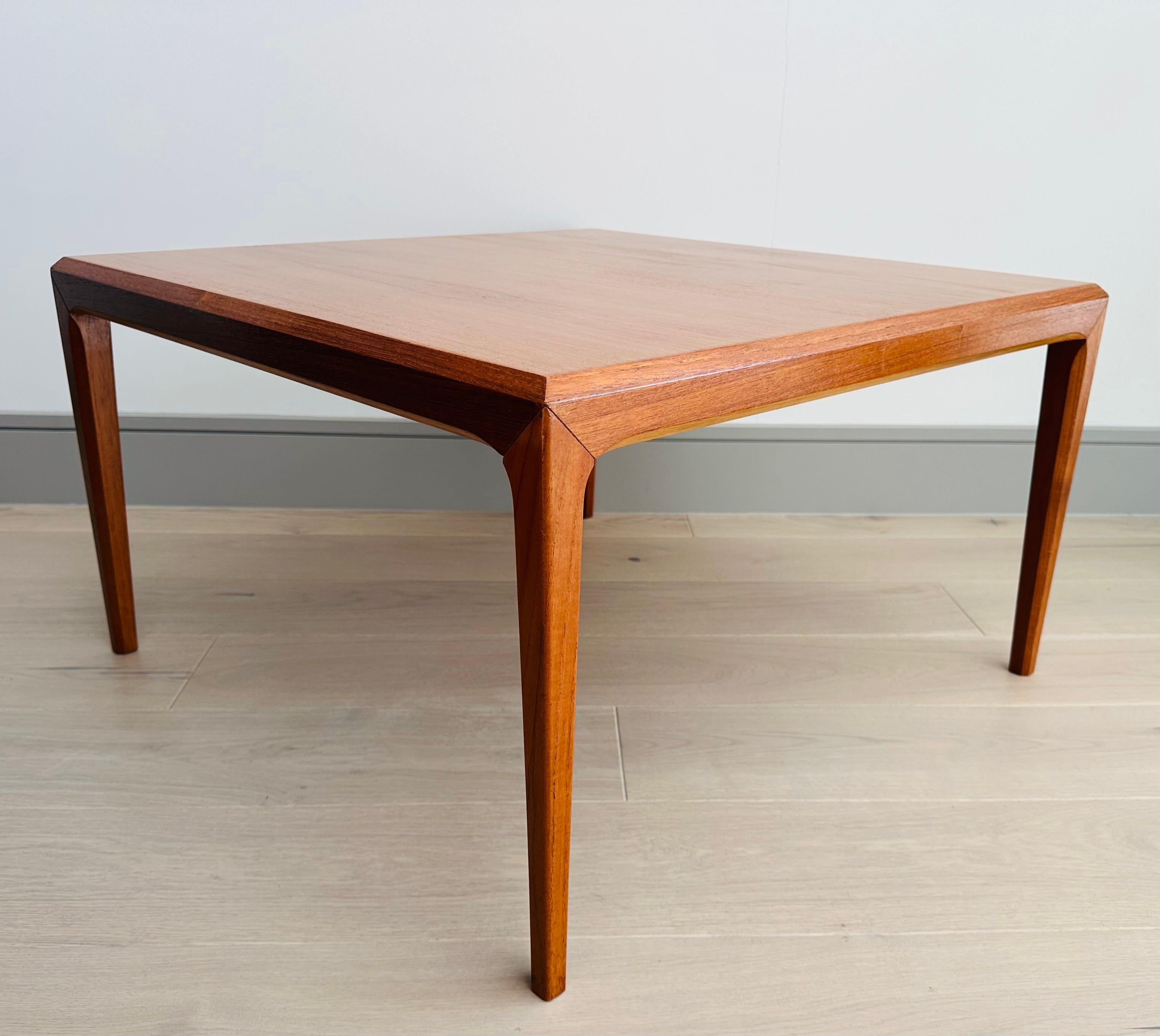 1960s Danish teak square low coffee table designed by Johannes Andersen and manufactured by Silkeborg Furniture.  The coffee table features chamfered edges and feature joints with a slight gap where the legs meet the table top.  The chamfered