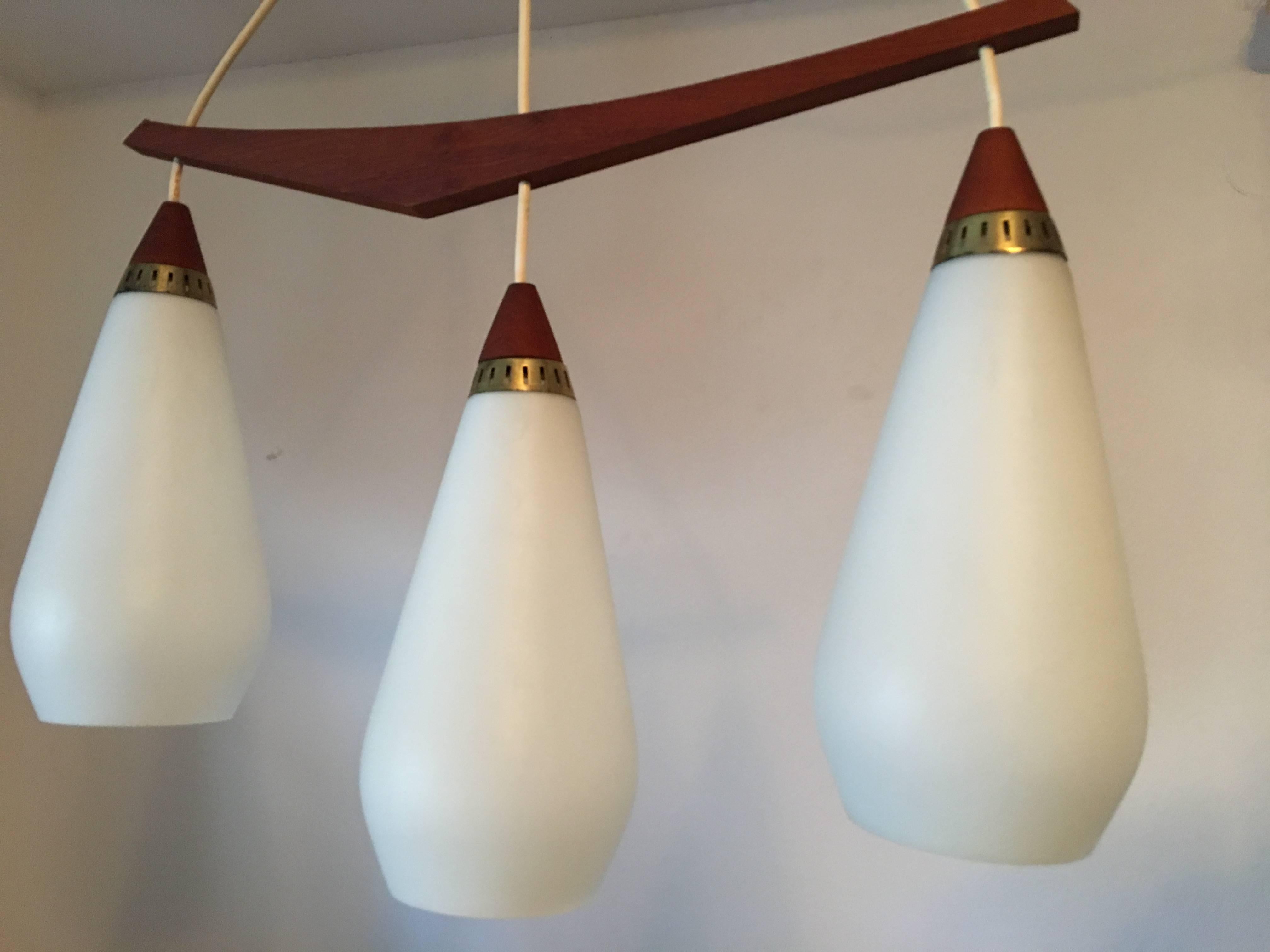 Danish modern chandelier made of lovely Teak with three milk glass lights. With its clear and sharp form it reflects the beautiful interplay between the wood and the lit up milk glass. A true representation of a classic 1960s design. It requires