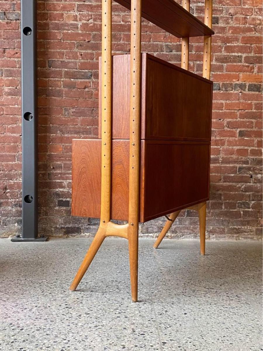 We are thrilled to present our finest modular shelving unit discovery yet: an exquisite freestanding creation by Kurt Ostervig from the 1950s. This stunning piece boasts a floating credenza, a drop-front secretary desk, and a pair of adjustable