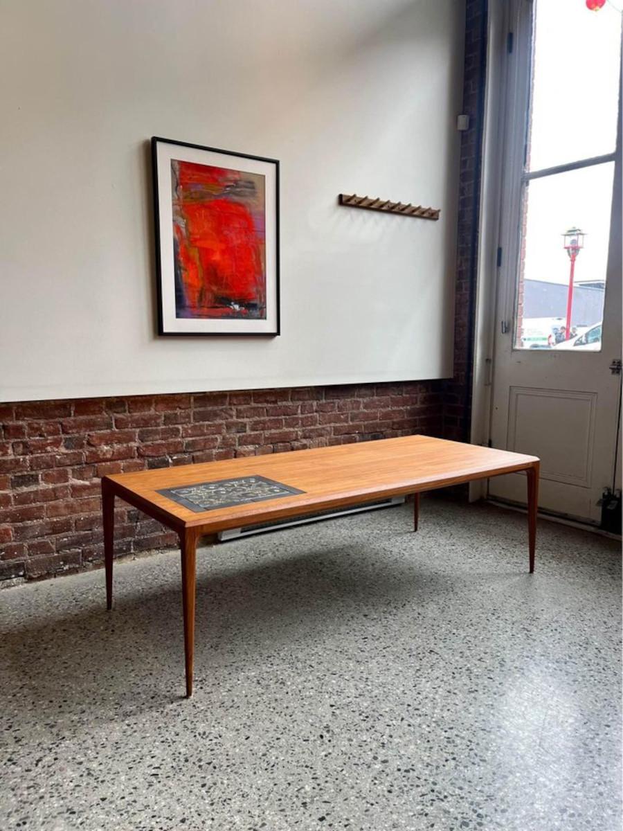 Ti presentiamo il tavolino danese in teak e piastrelle degli anni '60 di Johannes Andersen, realizzato per CFC Silkeborg. Adornato con intricate piastrelle Royal Copenhagen, emana raffinatezza e presenta un bordo smussato che aggiunge eleganza al