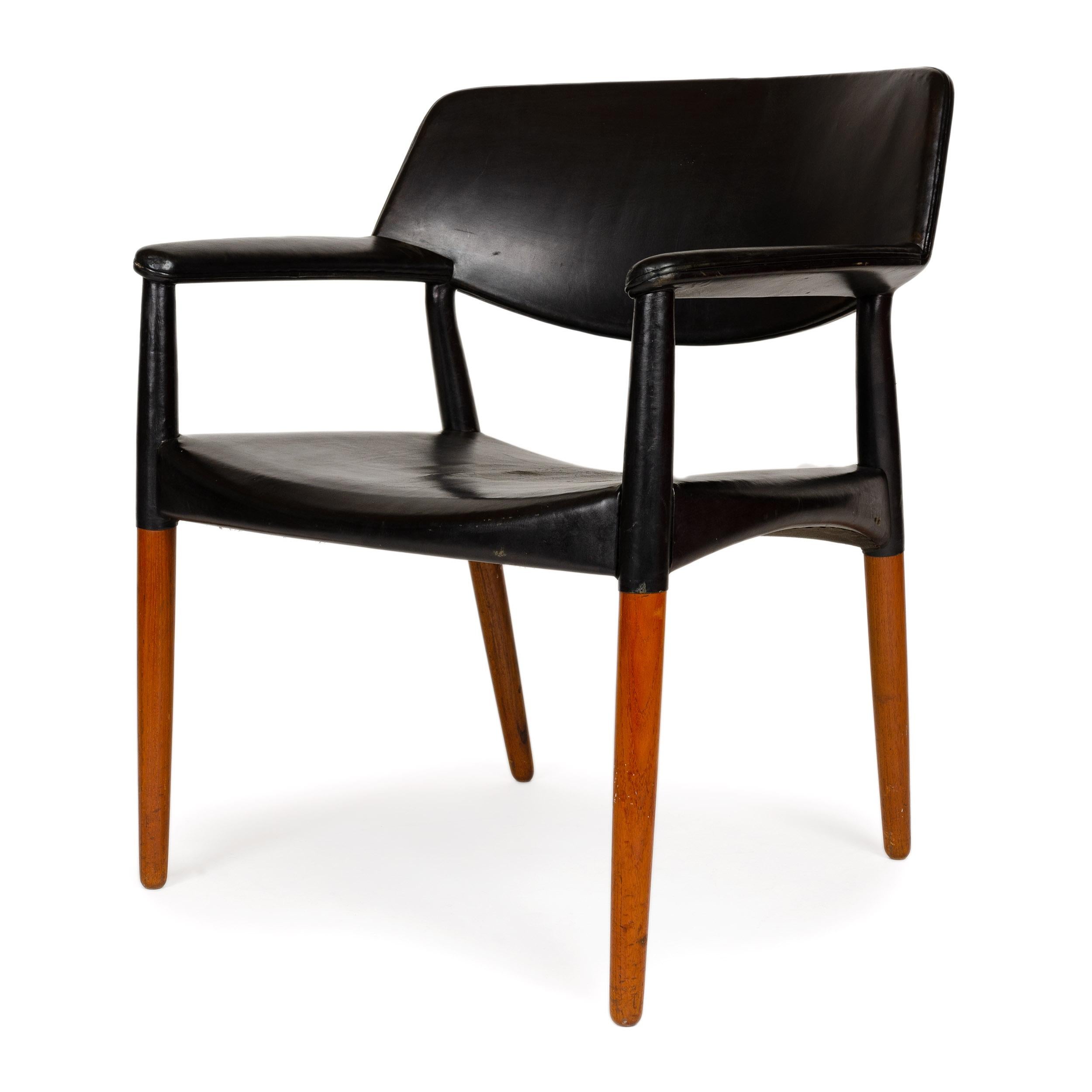 A comfortably wide (27.5’’) conference chair in solid teak and black leather. The designers characteristically clad the upper half of the chair in black leather while the exposed wood of the lower half is in natural teak. A gentle curve under the