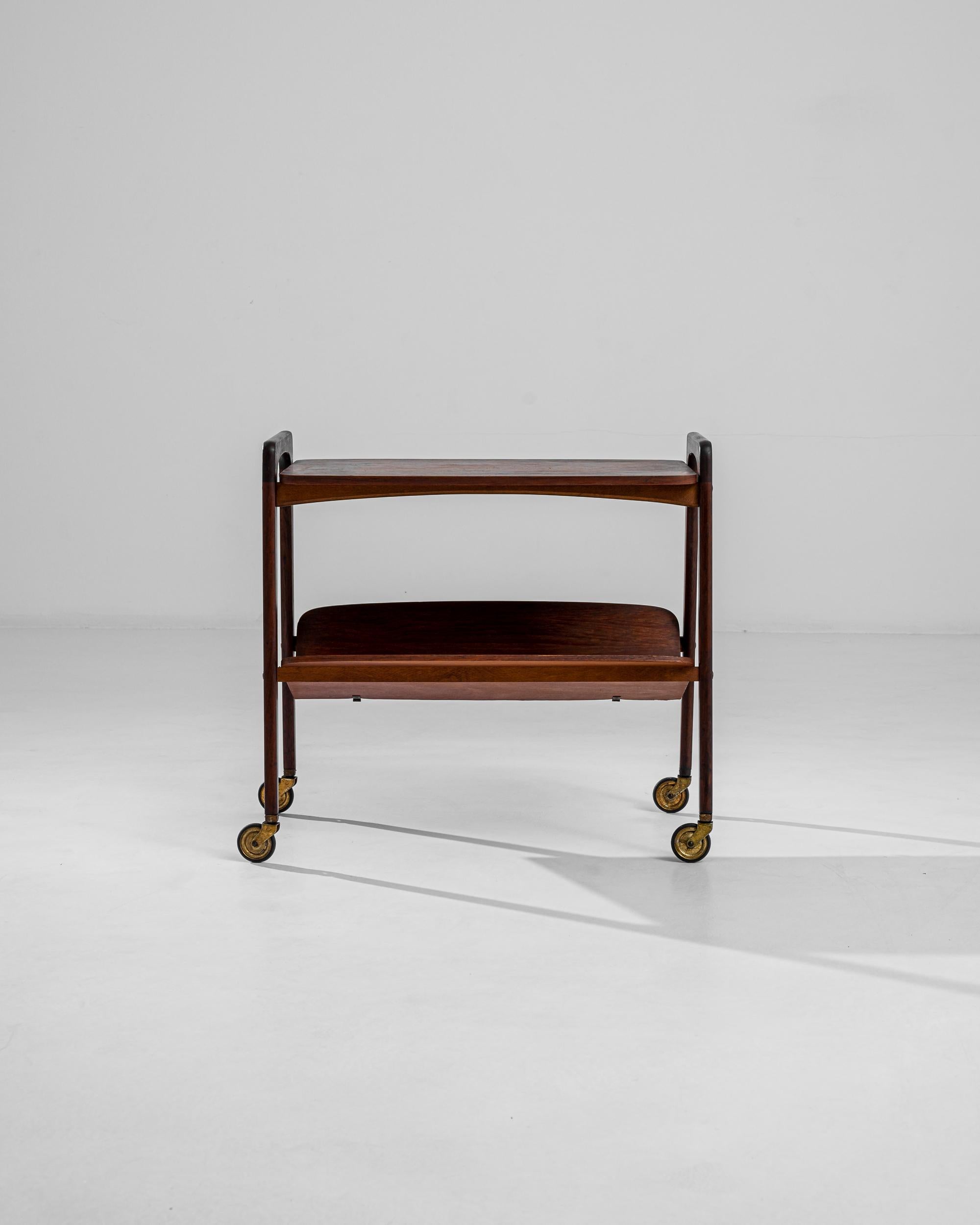 Discover the epitome of mid-century craftsmanship with this exquisite 1960s Danish Teak Bar Cart, a testament to timeless elegance and functional design. The rich, warm hues of teak wood evoke a sense of classic sophistication, beautifully