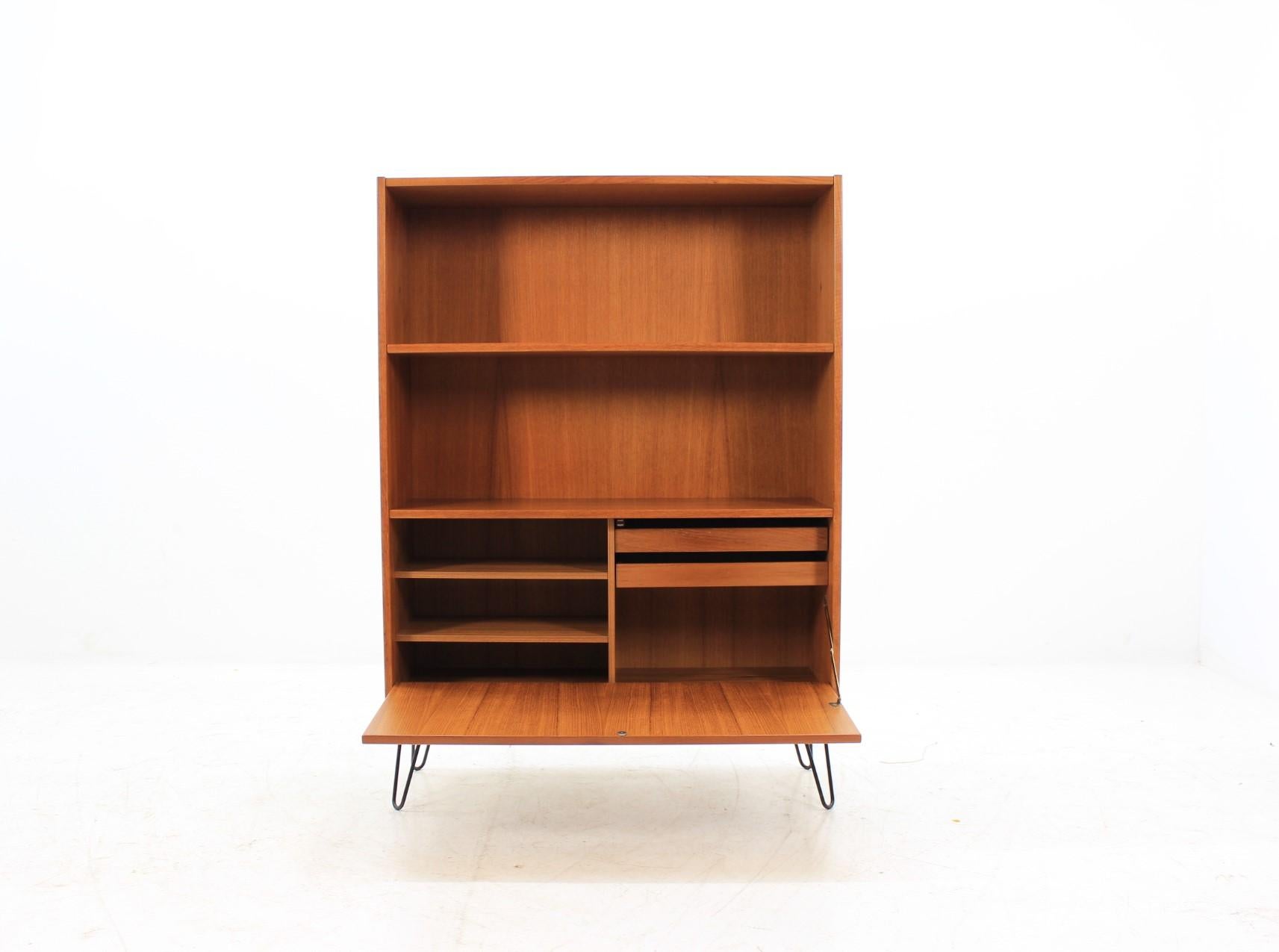 This cabinet/bookcase features one doors, shelves and two small drawers. The hairpin iron legs were added afterwards. This item was carefully refurbished.