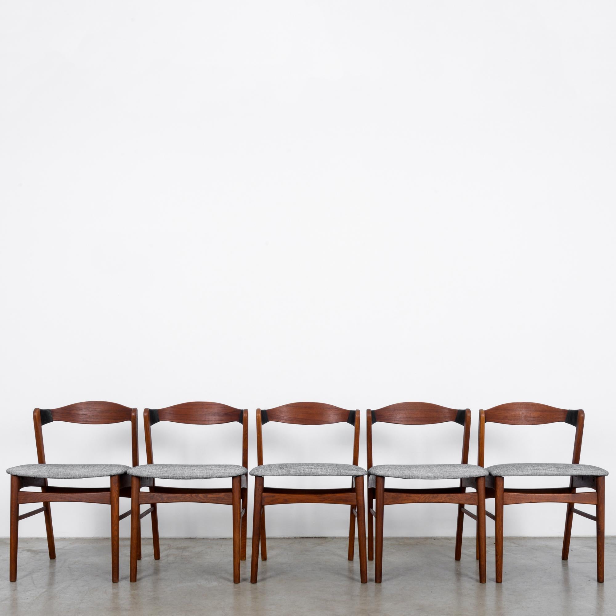 This set of five modern upholstered teak chairs from Denmark—circa 1960—features black accents on swooping seat backs lightly hovering over seats re-upholstered in textured gray, like a 1950s black and white star. Simple strut linking the softly