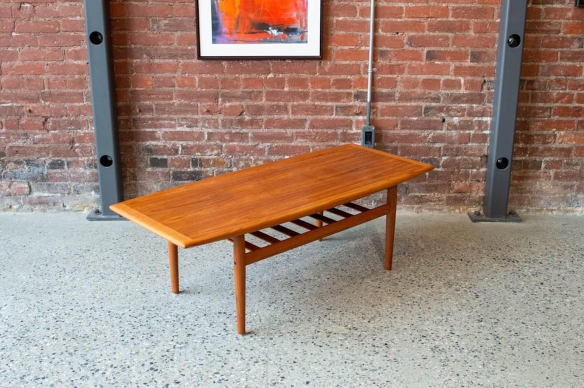 An epitome of Danish modern design, this creation by Grete Jalk showcases a gracefully sculpted surface, upheld by subtly tapered legs, and enhanced by a practical lower tier crafted from solid teak slats. Originating from Denmark in the 1960s, this