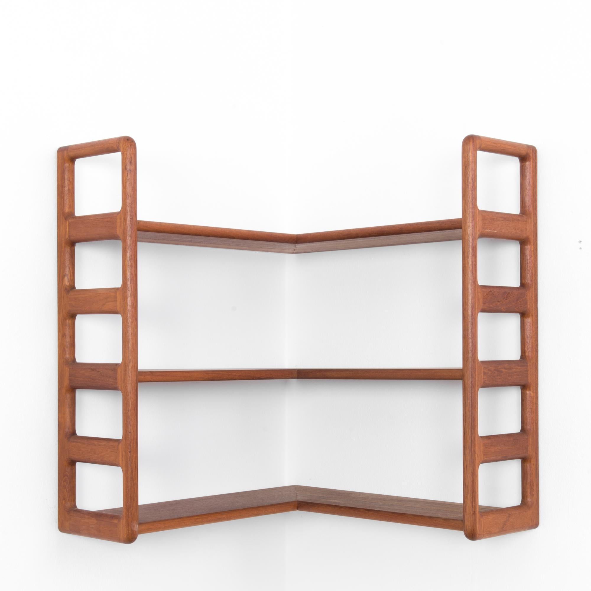 This teak corner wall shelf with a warm tone and beautiful wood grain was made in Denmark, circa 1960. This piece features three shelves and ladder-like ends. Rounded edges balance the clean lines of the shelf, showcasing the refined elegance of