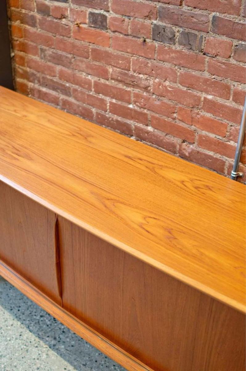 We are delighted to present our newest addition to our collection: a remarkable teak credenza crafted by Svend Madsen for SM Møbler, showcasing the finest vintage Danish craftsmanship. This piece boasts an elegantly curved front edge, a spacious