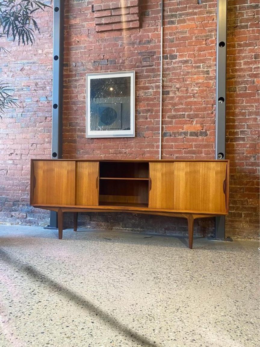 Discover this magnificent Danish teak credenza, a design marvel by Knud Nielsen from the 1960s. It boasts four sliding doors, a spacious central storage cabinet, versatile adjustable shelving, and a left-sided array of drawers. Knud's distinctive