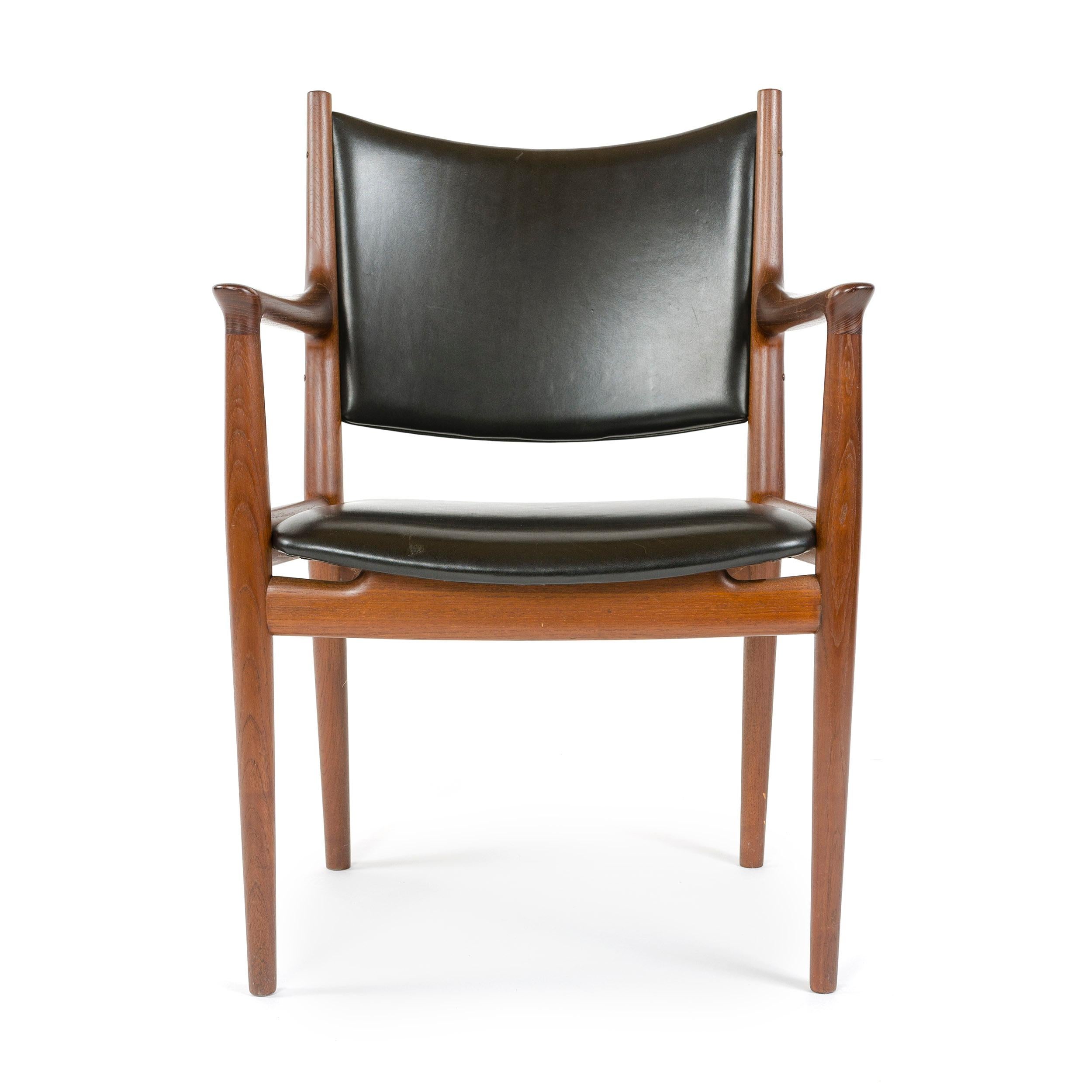 An elegant handcrafted dining chair, having an exposed teak frame and leather upholstery.