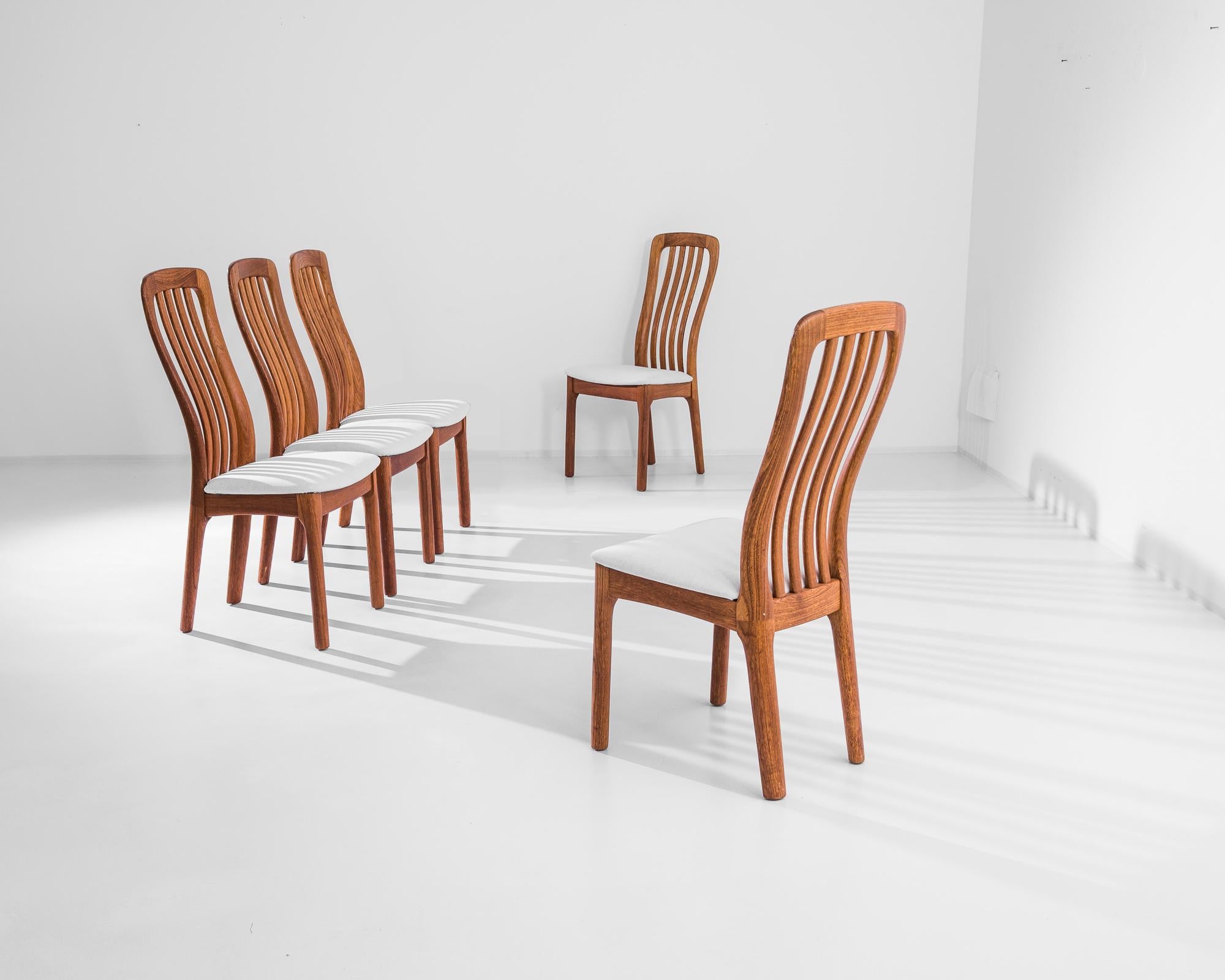 A set of five Mid-Century Modern wooden dining chairs from 1960s Denmark. The fluid ripple of the backrest gives an inherent liveliness to the silhouette, counterbalanced by the gentle taper of the back leg. Warm, caramel-colored wood frames a seat