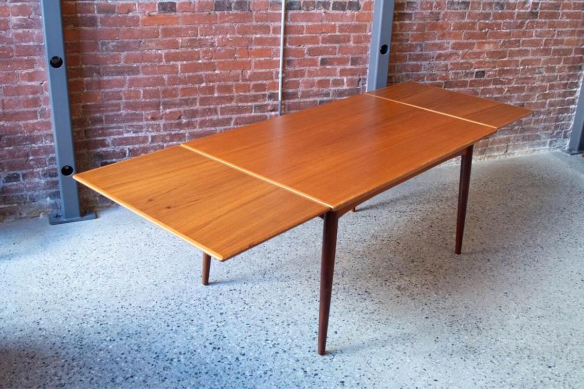 Freshly emerged from restoration, this charming Danish teak dining table hails from the esteemed Gudme Møbelfabrik, crafted during the 1960s. It stands out among vintage draw-leaf dining tables, showcasing gracefully splayed legs, knife-edge leaves,