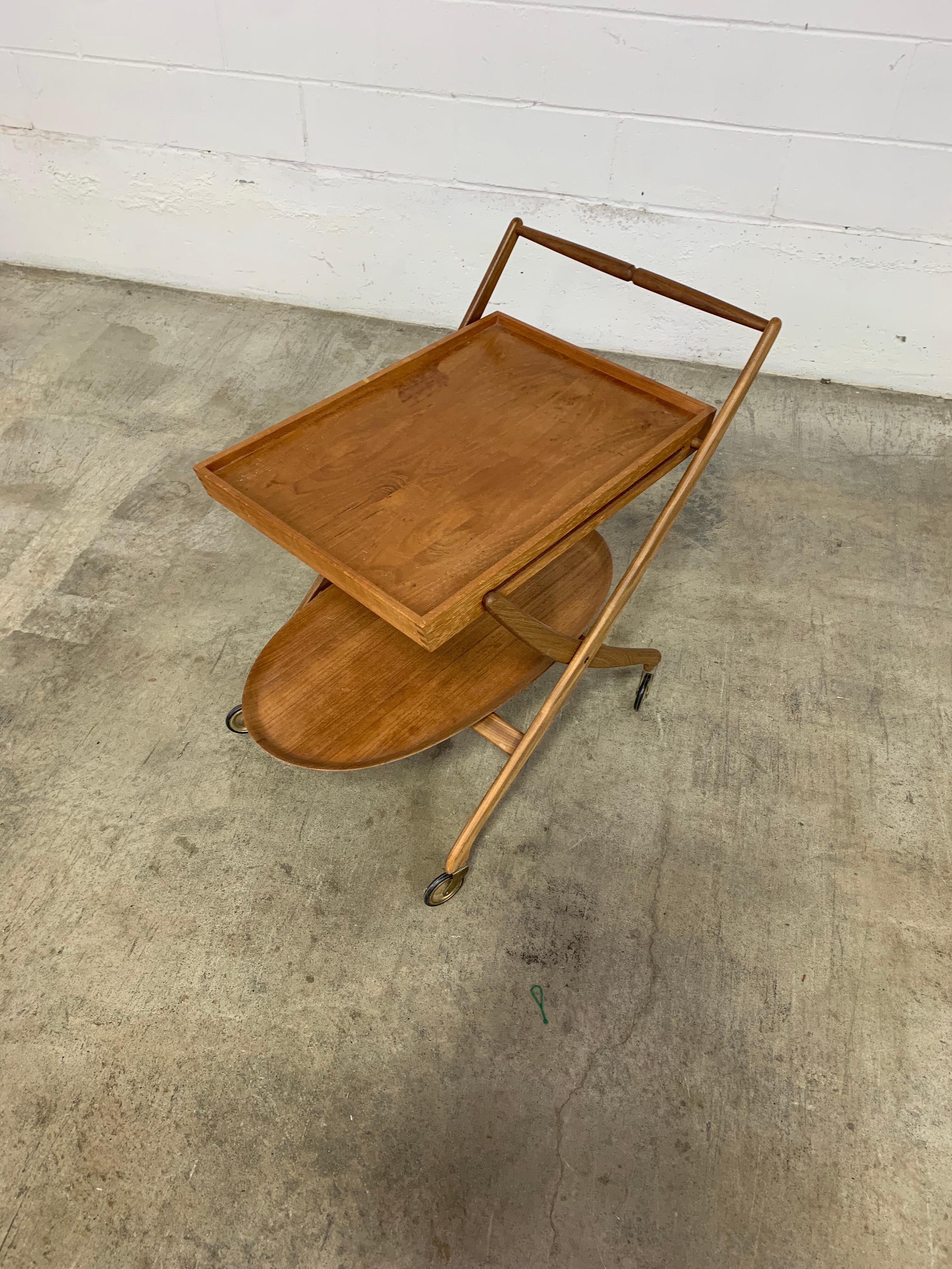 A sculptural 1960s Danish teak serving cart that’s as functional as it is beautiful. Designed with elegance and ease in mind, it features a removable tray, gracefully curved frame, and smooth brass-accented casters. The folding design allows for
