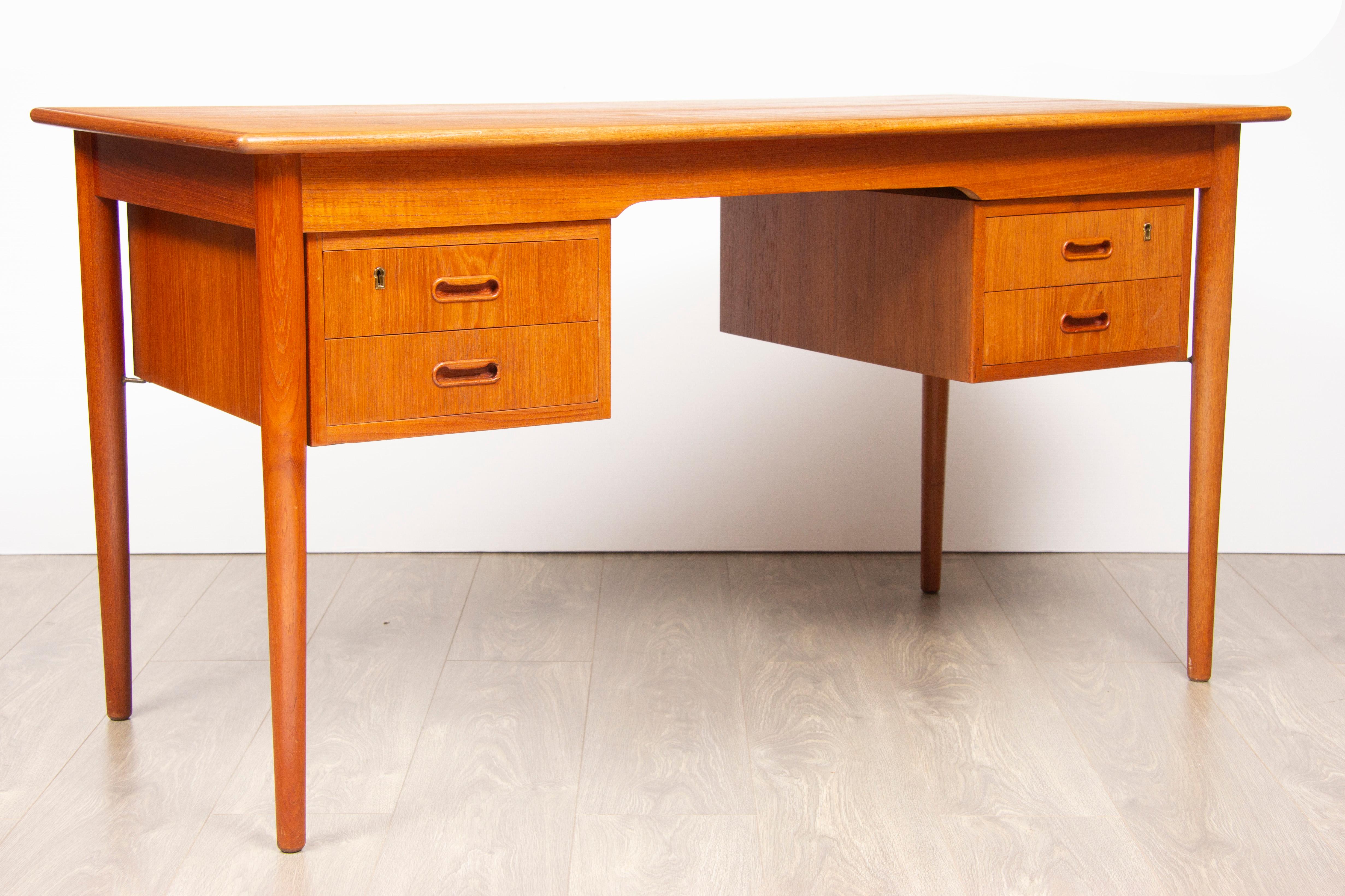 1960s Danish teak desk with four feature drawers suspended beneath connected to the legs with a brass fixture holding them in place. Each drawer has a central recessed handle and brass key hole sadly the keys are missing. The desk has been