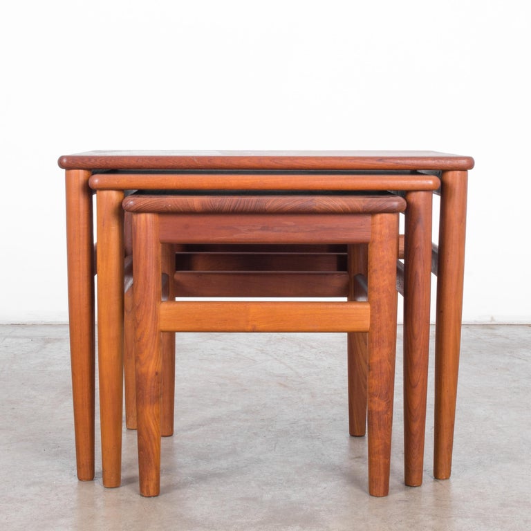 This set of three teak nesting tables was made in Denmark, circa 1960. The tables display the warmth and simplicity of Danish modern design. Their geometric forms are softened by the rounded edges and tapered legs. The high-quality teak has a