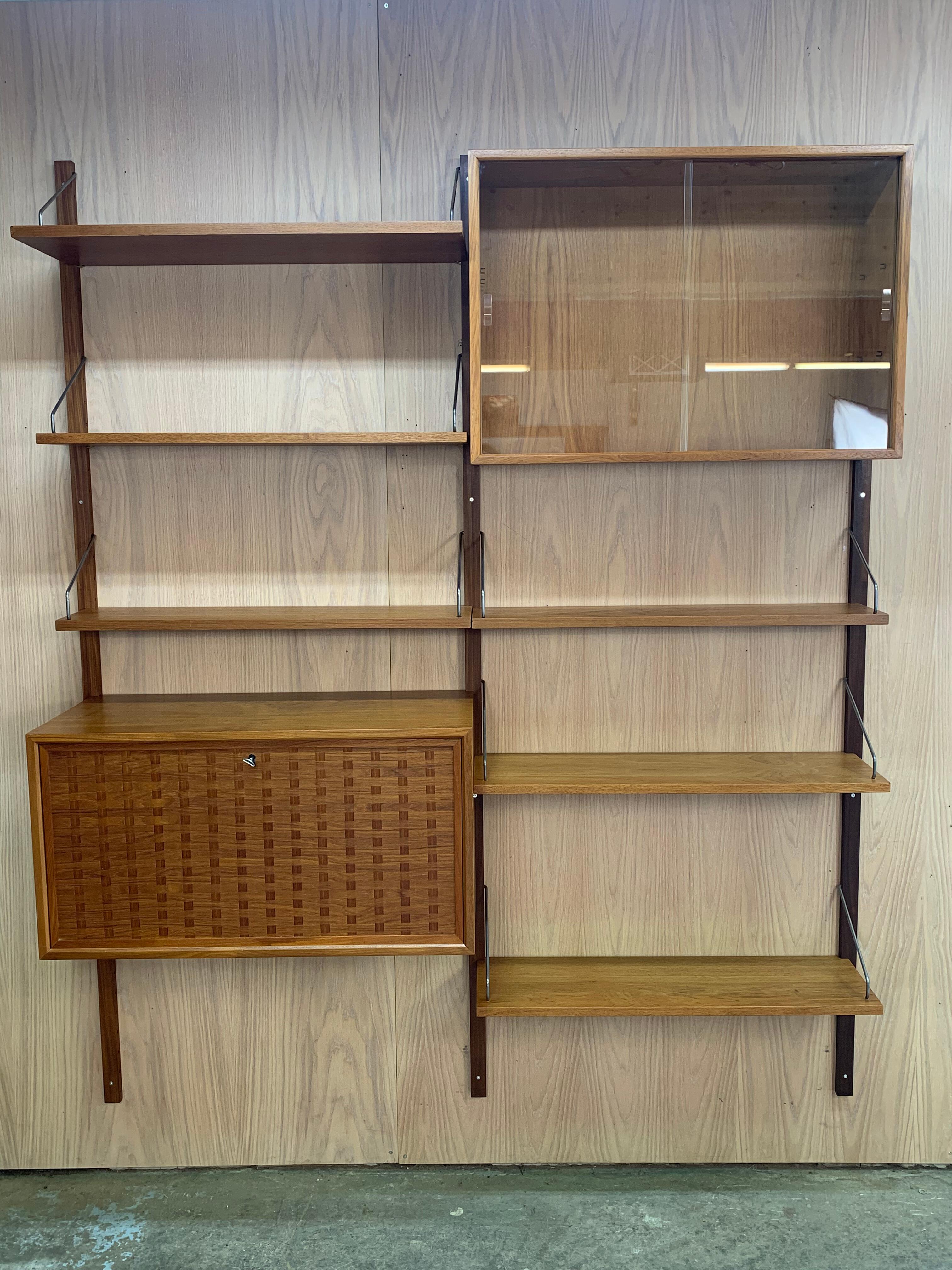 Este mueble alto danés de los años 60, un bello ejemplo restaurado del emblemático Royal System de Poul Cadovius, ejemplifica la elegancia y funcionalidad del diseño moderno escandinavo. Fabricada en madera de teca veteada, tiene componentes