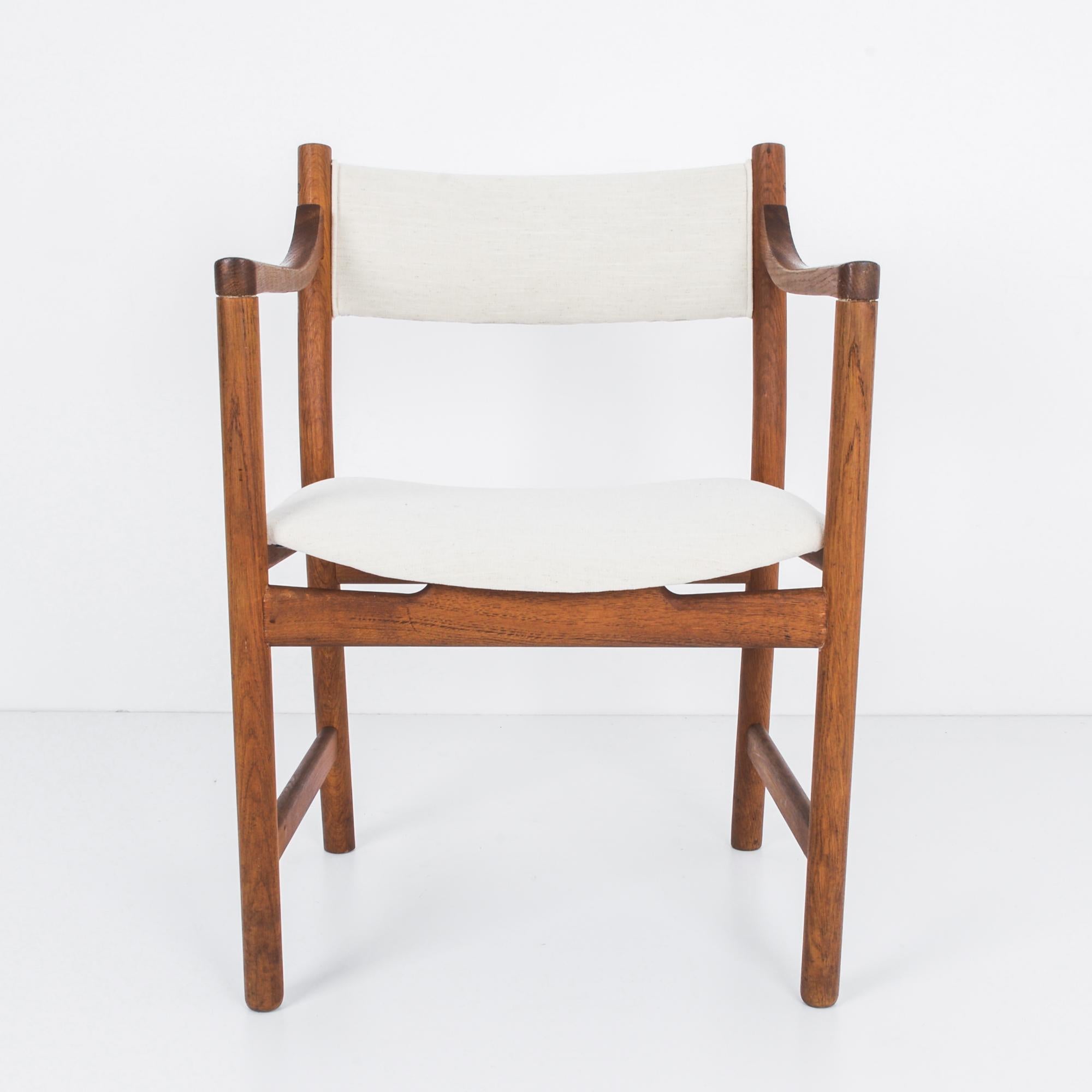 A teak armchair from Denmark, circa 1960s. An upright shape with a gentle angularity; the slant of the back legs counterbalances the soft recline of the backrest and the subtle upwards tilt of the seat. An upholstered seat and backrest in a natural