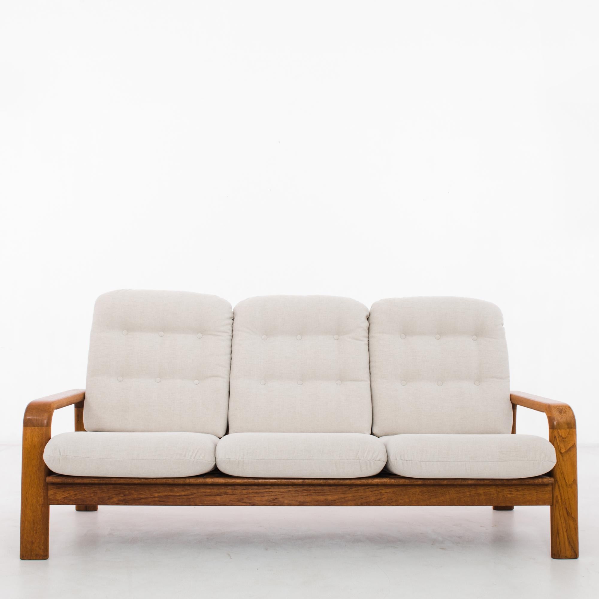 A teak upholstered sofa from Denmark, produced circa 1960. Following in the Functionalist mode of Scandinavian Modernism, this vintage three person sofa highlights the clean lines of its bright teak frame supporting six plush, off-white cushions.