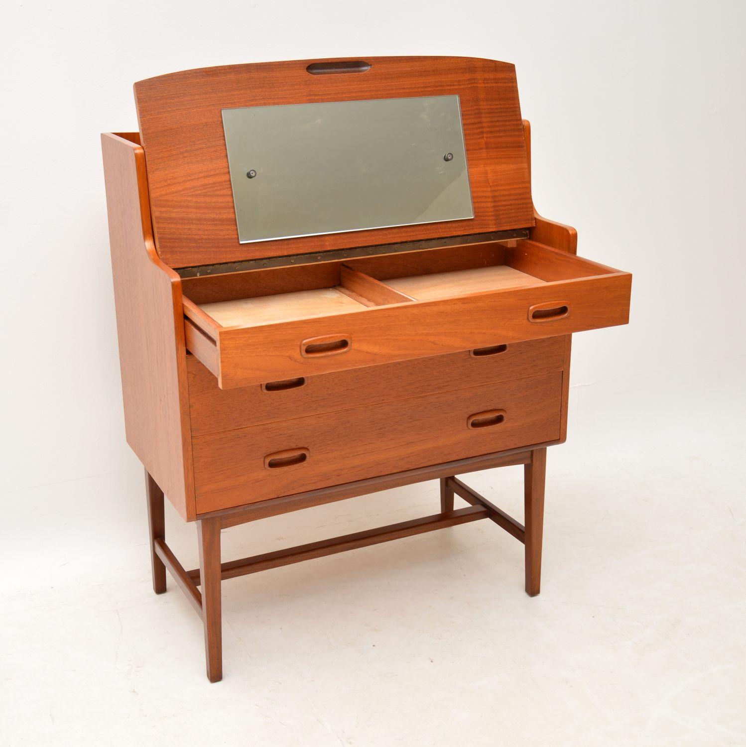 A stylish and practical vintage teak vanity bureau, this dates from the 1960s. It has a fantastic mechanism, the top drawer is a dummy that pulls out and flips up to reveal a mirror and storage space. This can equally be used as a writing bureau or
