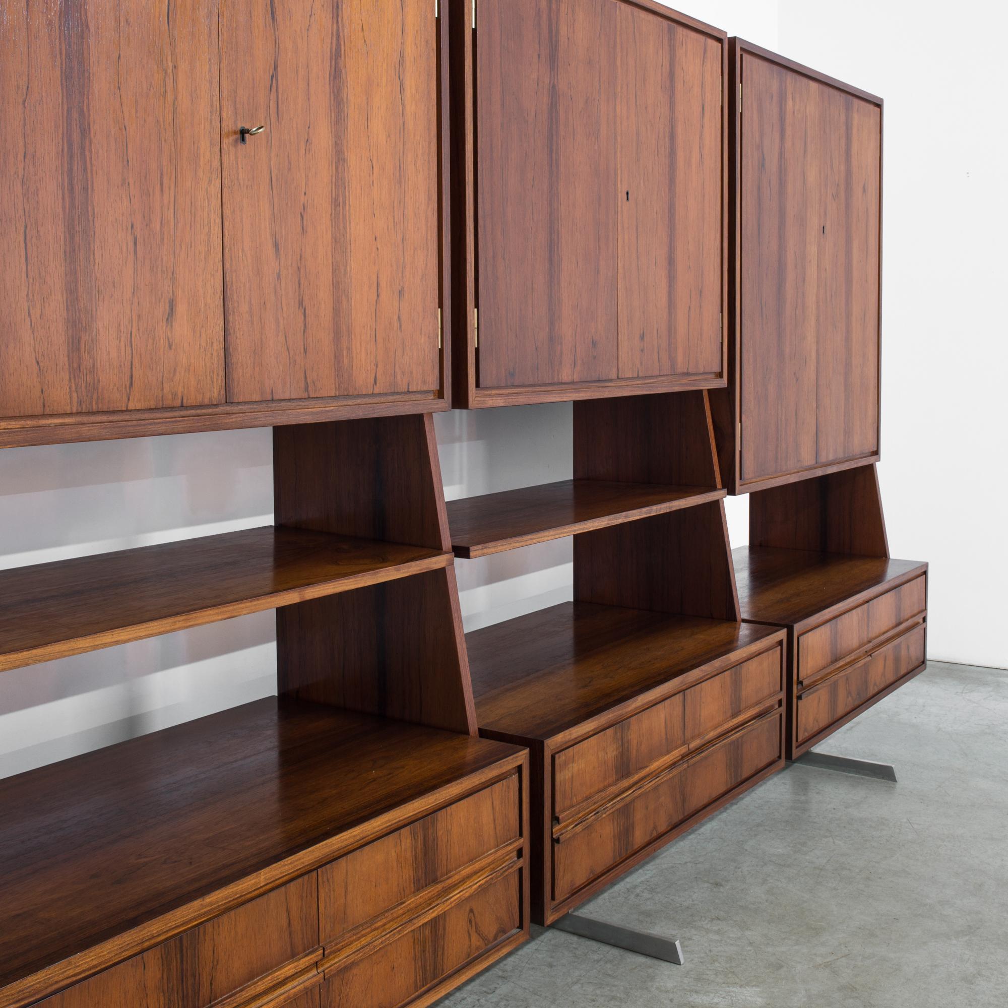 A modern teak wall unit from Denmark, circa 1960. This mammoth triptych of a wall unit has three double door cabinets, six shelves, and twelve drawers all balanced delicately on three metal feet. Hard to believe that a piece of this size is able to