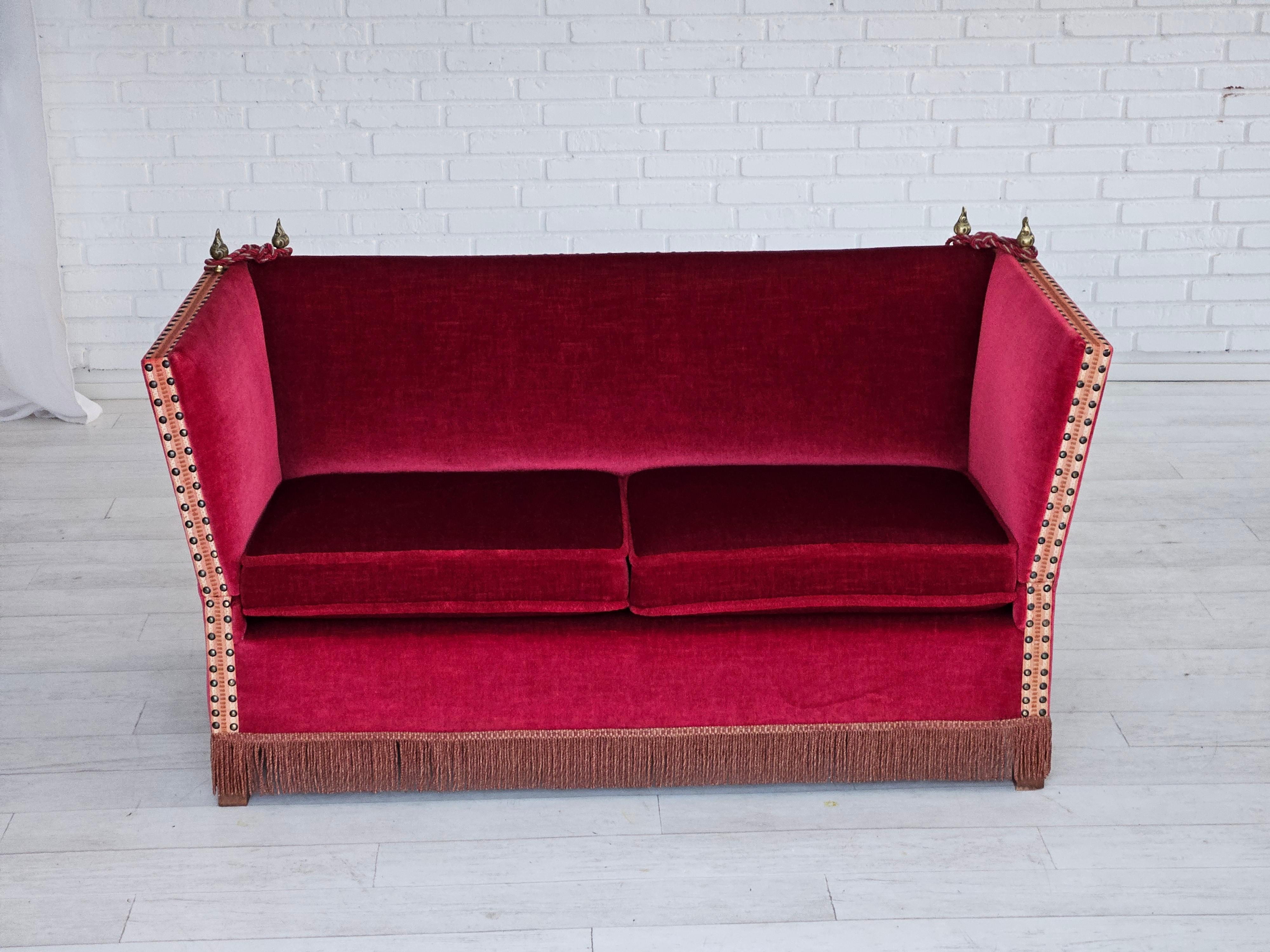 1960s, Danish drop-arm 2 seater sofa in original very good condition: no smells and no stains. Original cherry-red furniture velour, ash wood legs, cast brass pears. Springs in the seat cushions. Adjustable armrests (adjustment lever under the back