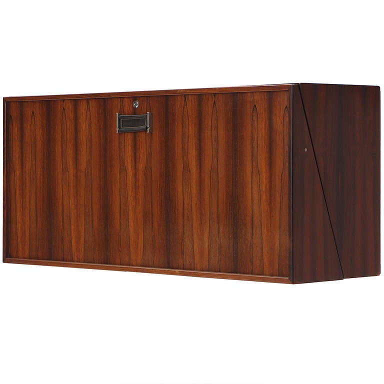 A beautiful wall-mounted bar in expressive rosewood having a drop-down shelf revealing recessed bottle holders and floating shelves and drawers with flush chromed pulls. This well-engineered and finely detailed bar presents a dramatic angled side