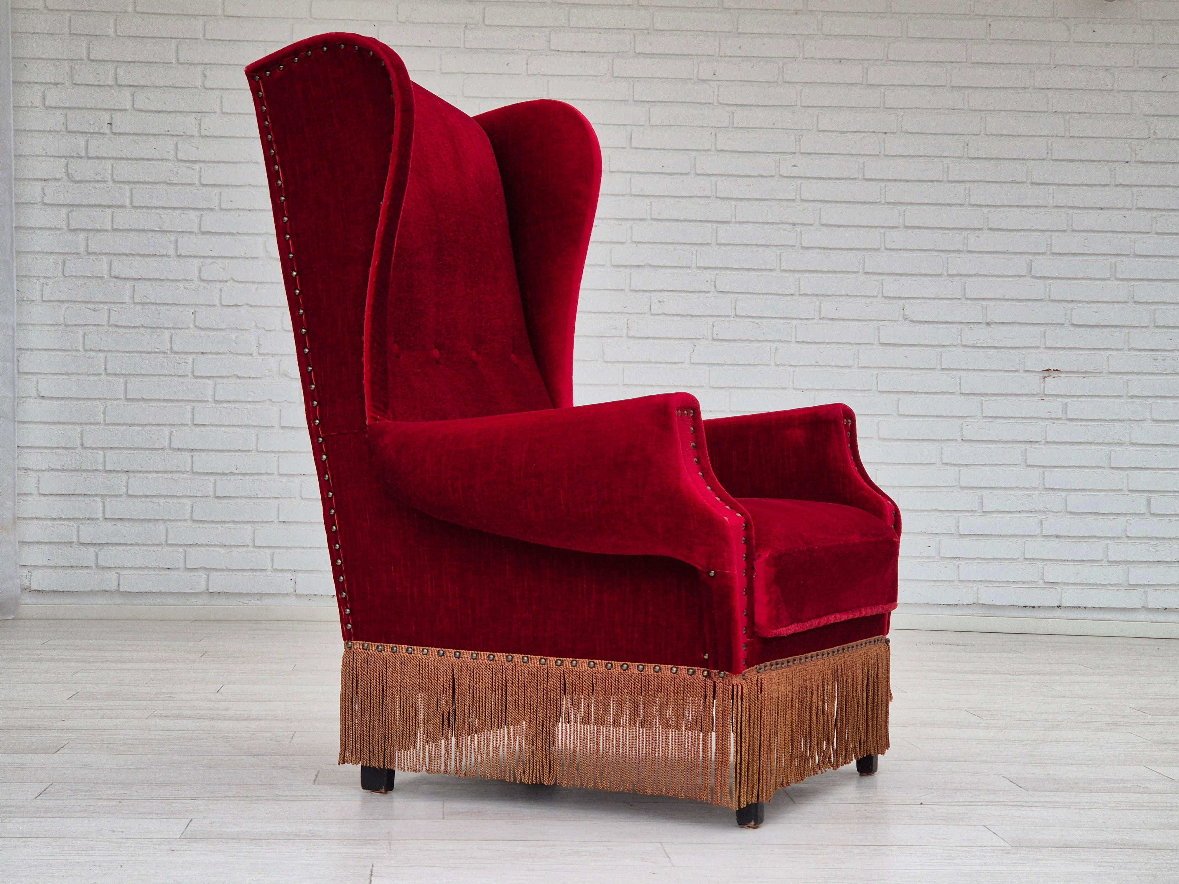 1960s, Danish wingback armchair in original very good condition: no smells and no stains. Cherry-red furniture velour, oak wood legs. Springs in the seat. Manufactured by Danish furniture manufacturer in about 1960s.