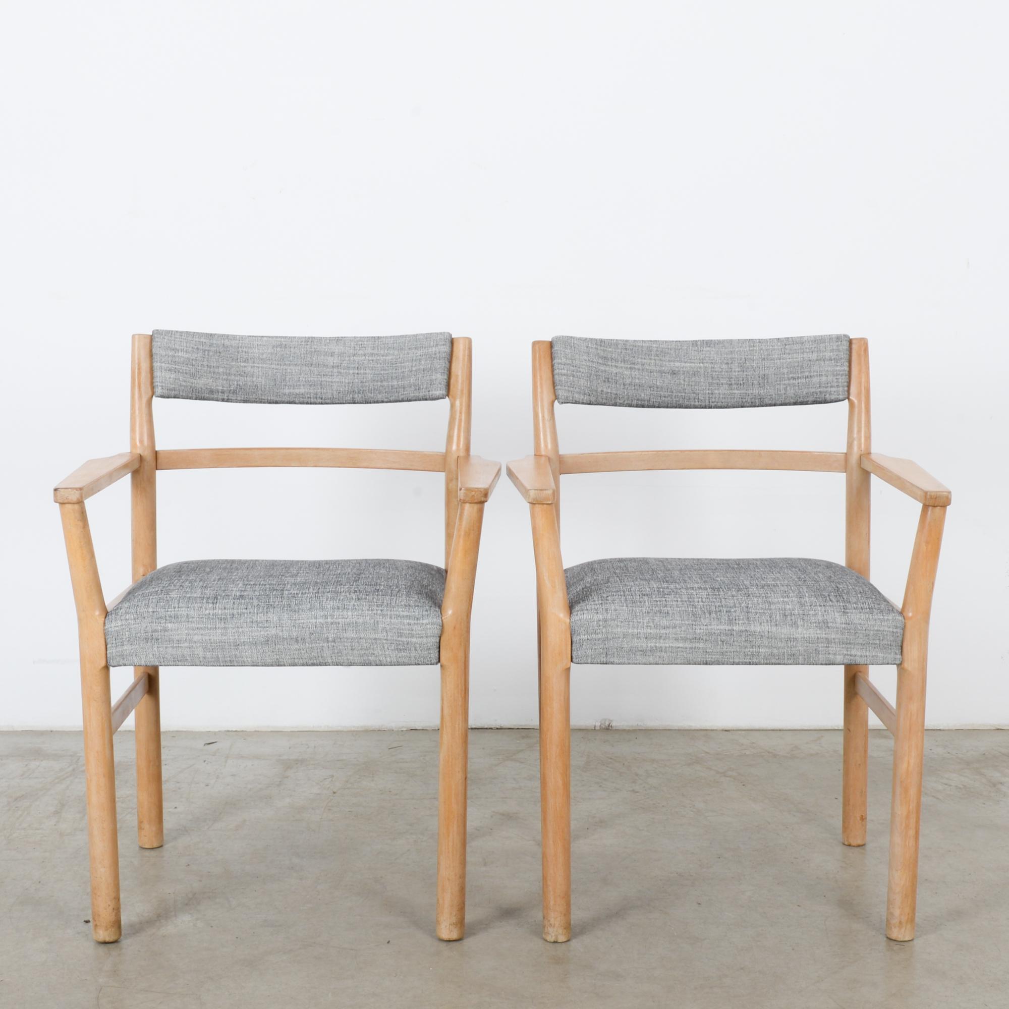 A pair of upholstered armchairs from Denmark, circa 1960. The frame is made of light, sandy wood with a soft polish, and the seat and backrests are upholstered in a gently striated pigeon gray. Broad armrests and a gentle tilt to the backrests