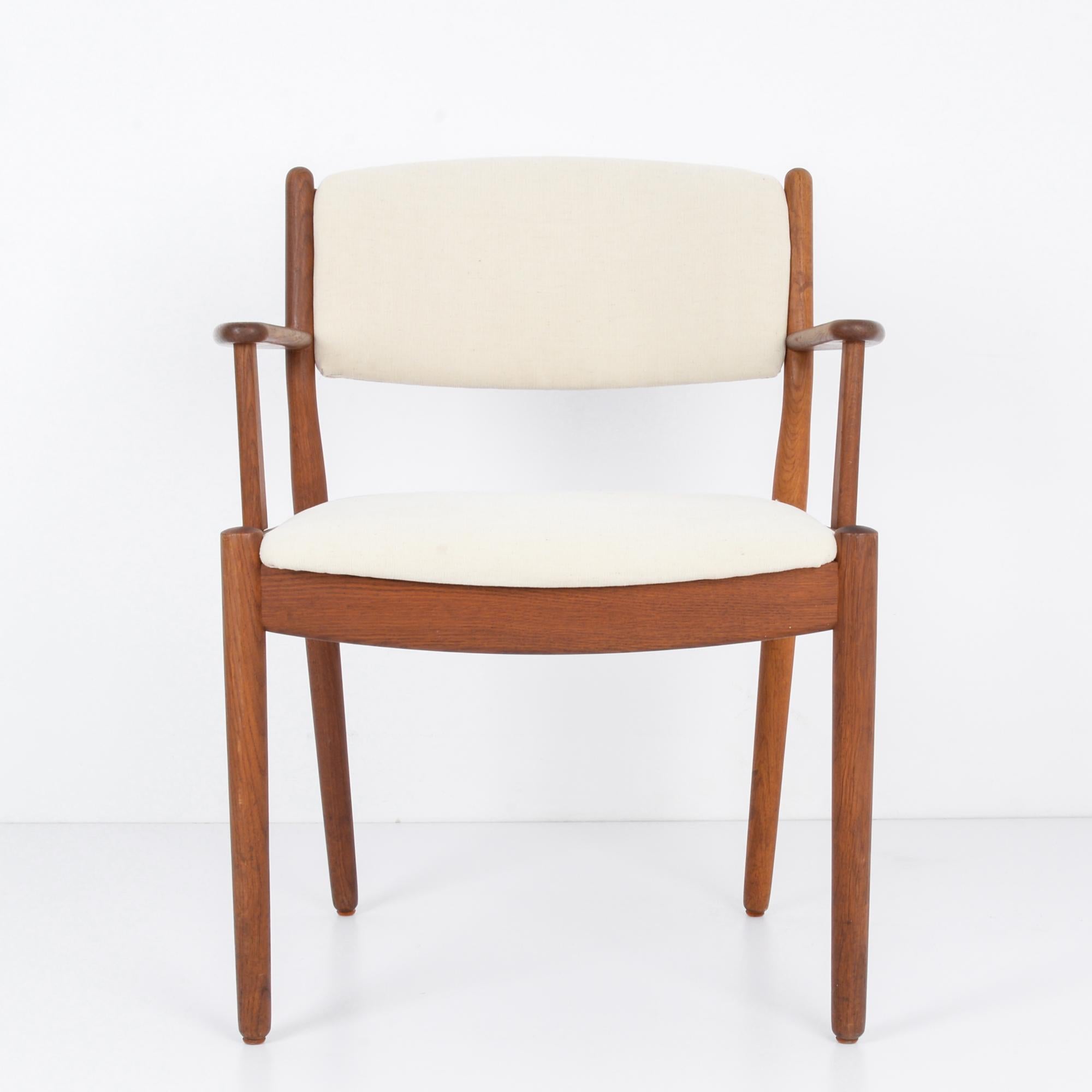 This wooden armchair with an upholstered seat and back was made in Denmark, circa 1960. Designed in the Danish modern style, the chair emphasizes function, comfort, and warmth. It features a wide seat, slightly tapered legs, and angular armrests.