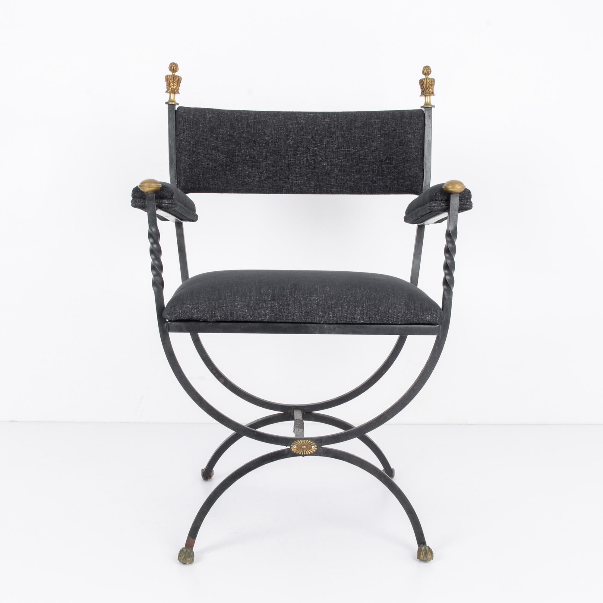 A metal armchair with an upholstered seat and back rest from Denmark, circa 1960. A frame of wrought black metal, pommelled with gold accents, creates a stark Silhouette. The seat rests on an arrangement of two inverted semi-circles, united by a