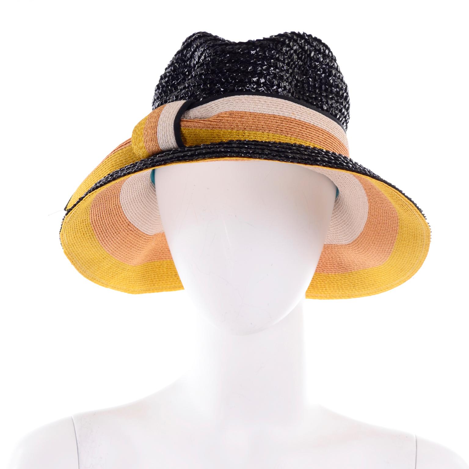 This is a deadstock vintage Yves Saint Laurent straw hat with the original tags still attached. This is a great glossy black woven straw hat with yellow, tan, and cream striped ribbon detail.. The underside of the hat is the same striped colors as